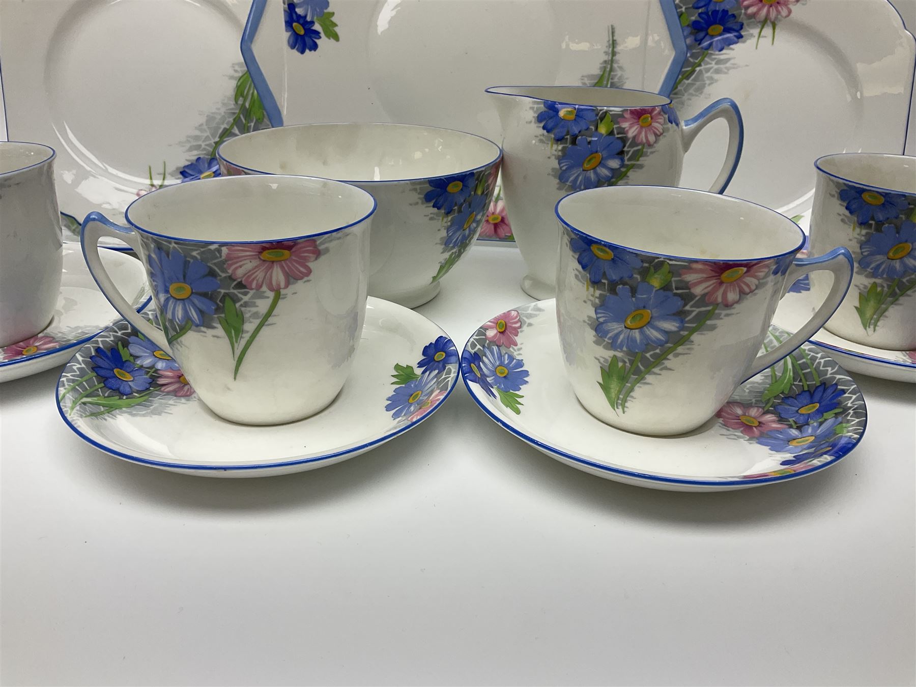 Shelley Strand shaped tea wares, decorated with blue and pink daisies upon a white ground, comprising four teacups, four saucers, three tea plates, milk jug, sugar bowl and cake plate, all with printed green mark beneath and painted pattern no 12216