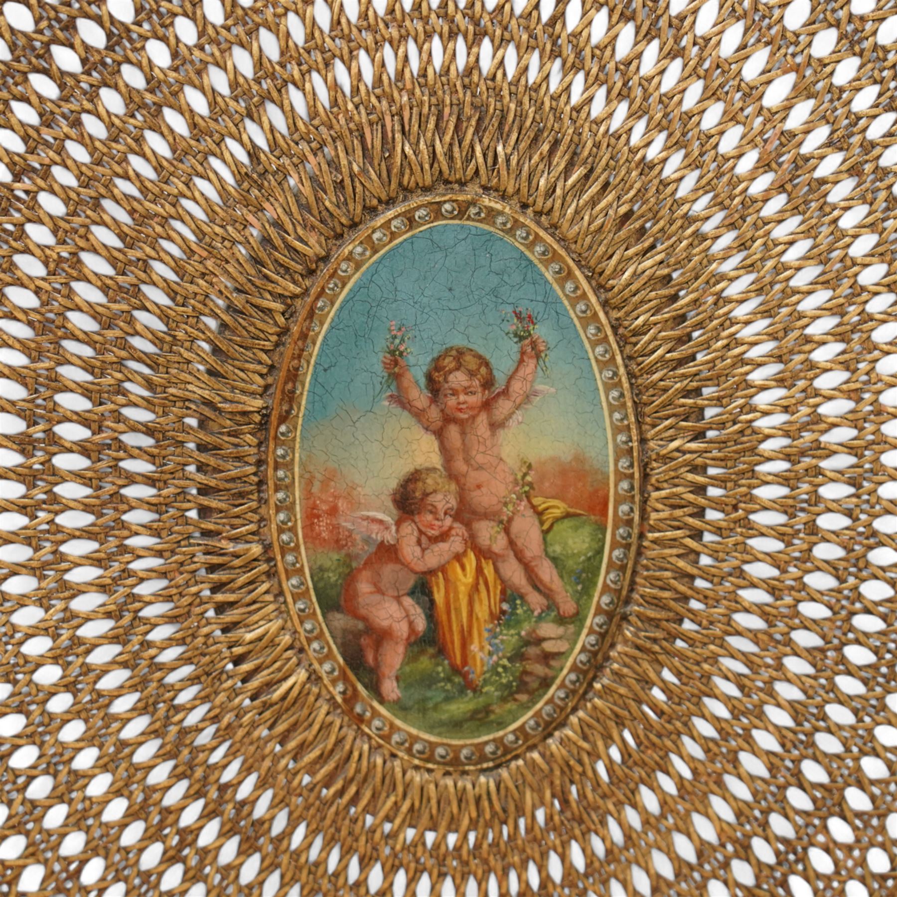 Pair of Edwardian Hepplewhite Revival green-painted open armchairs, cane work shield back with central oval panel panted with putto set upon rocky landscape with water and trees, shaped and rolled arms enclosing cane work seat, on turned front supports decorated with acanthus leaves and draped festoons 