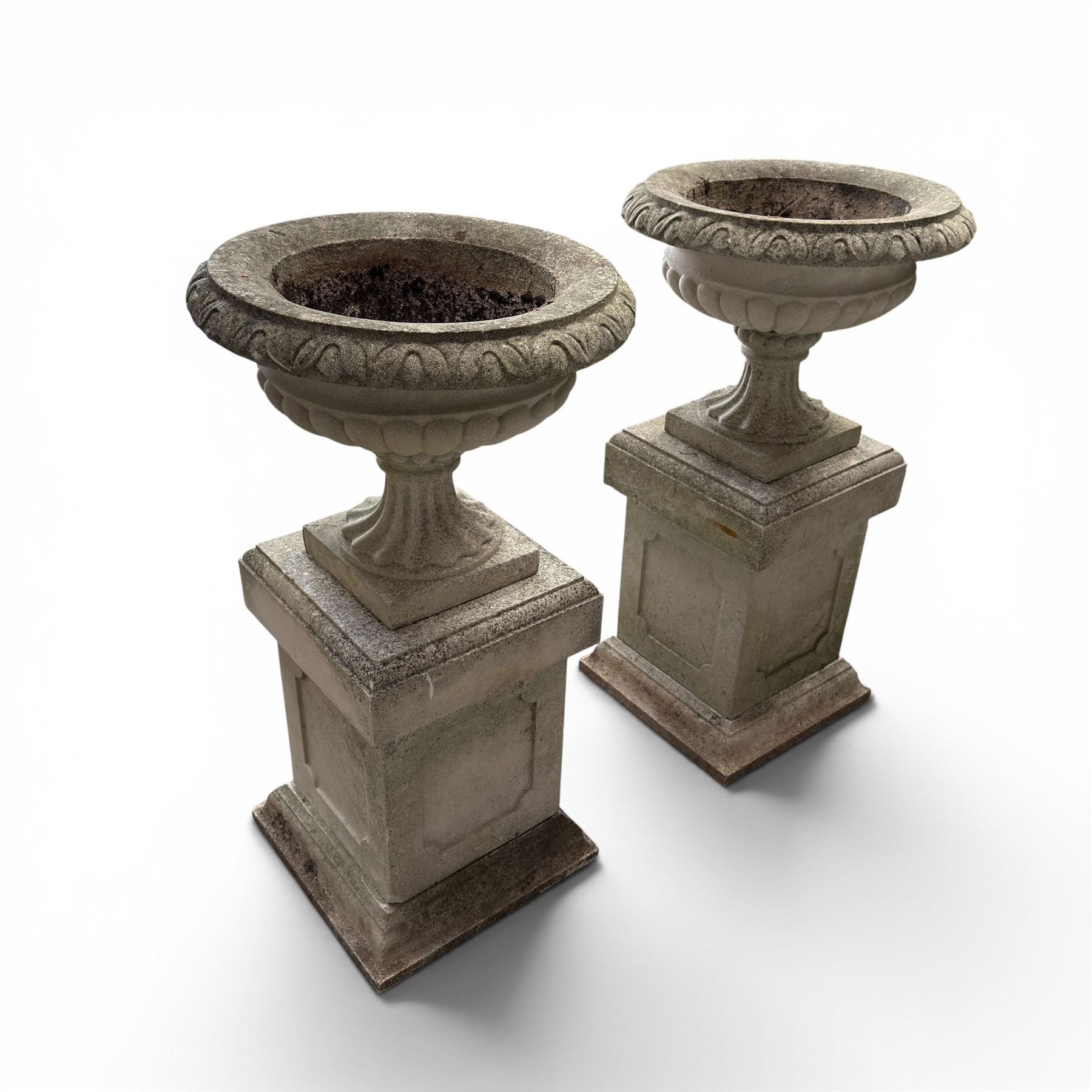 Pair of weathered cast stone Neoclassical design garden Kylix shape urns, foliate moulded rim over a gadrooned underbelly, the scalloped socle over a rectangular pedestal with faux-panelled sides, stamped with stylised ‘H’ monogram