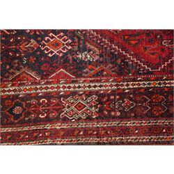 Large Persian Shiraz crimson ground carpet, the busy field decorated with a geometric pole medallion surrounded by stylised plant motifs with contrasting indigo spandrels and geometric-woven guard bands