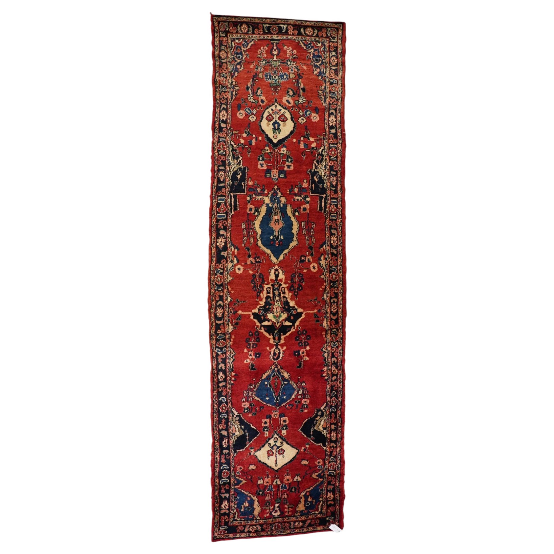Persian Hamadan runner rug, the vermilion ground decorated with a row of ivory and indigo medallions interspersed with stylised flowering plants, indigo spandrels, enclosed by an indigo floral border and narrow patterned guard stripes