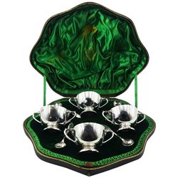 Set of four Edwardian silver open salts and salt spoons, the open salts of circular form with twin curved handles, upon a spreading circular foot, with later blue glass liners, hallmarked Wakely & Wheeler, London 1901, contained within a shaped fitted case with green silk and velvet lined interior, approximate total silver weight 8.64 ozt (268.9 grams)