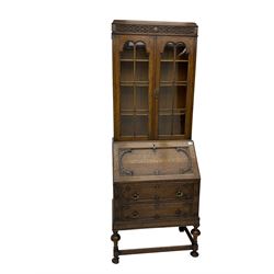Early to mid-20th century oak bureau bookcase, blind fretwork frieze over two astragal glazed doors, the fall front with foliate carved brackets enclosing fitted interior, fitted with two drawers, on turned supports joined by moulded stretchers