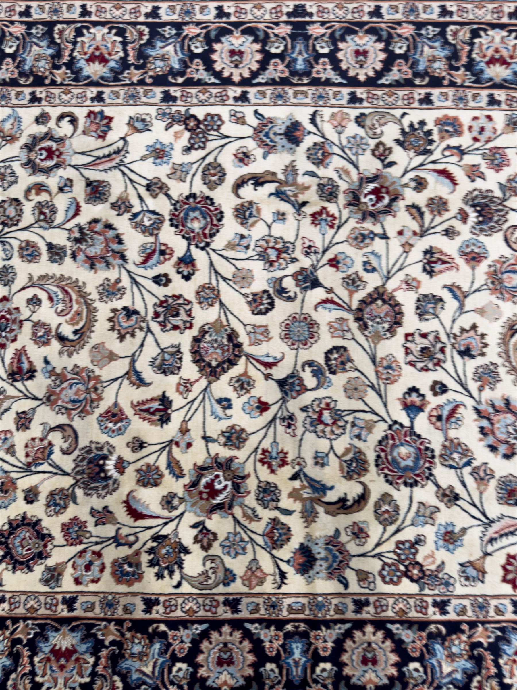 North East Persian Meshed hand-knotted rug, ivory field with scrolling vines, palmettes, and rosettes in shades of blue and brown, within a dark blue border of palmettes and flowerheads between multiple guard stripes, with cotton fringe ends  