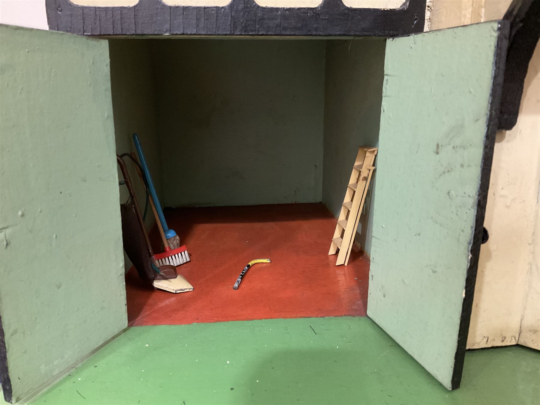 Large Tri-ang No.93 doll`s house in the 'Stockbroker's Range' c1935; two-storey double-fronted Tudor design, half timbered gables, two-storey bay windows, cream and mock shrubbery to front, opening metal framed windows with green shutters, red simulated tiled roof with chimney, integral garage with opening doors, front elevation has four hinged doors opening to reveal two bedrooms with fire places, living room, bathroom and kitchen with built in dresser and sink, entrance hall and staircase, side entrance with porch and seat and sun dial over on chimney stack; some wiring for electrical lighting; metal Tri-ang Toys disc verso; comprehensively furnished H66cm L117cm D43cm