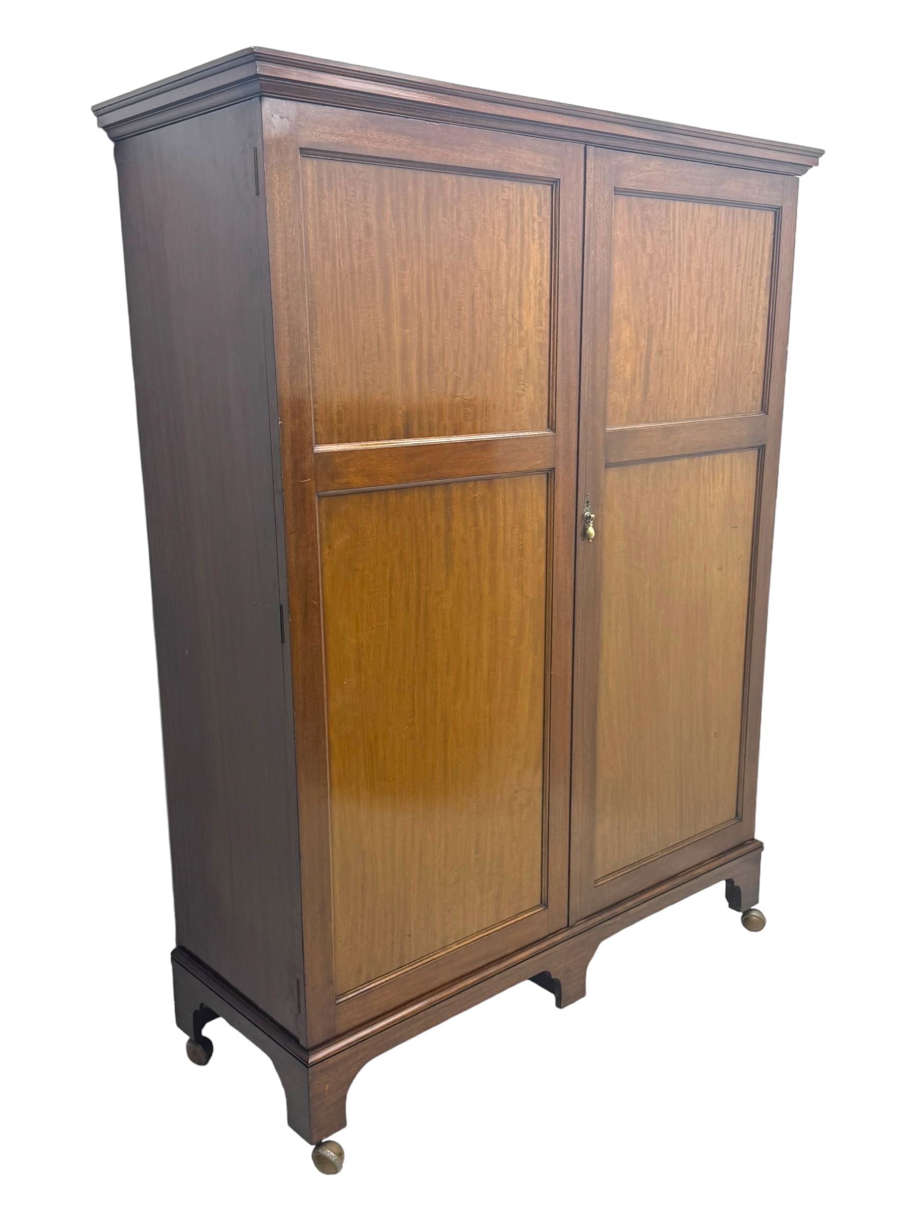 Wylie & Lochhead, Glasgow - early 20th century mahogany and satinwood double wardrobe, projecting cornice over panelled doors, interior fitted with mirrored door, shelves, drawers, hooks and hanging rail, raised on bracket supports with ceramic castors
