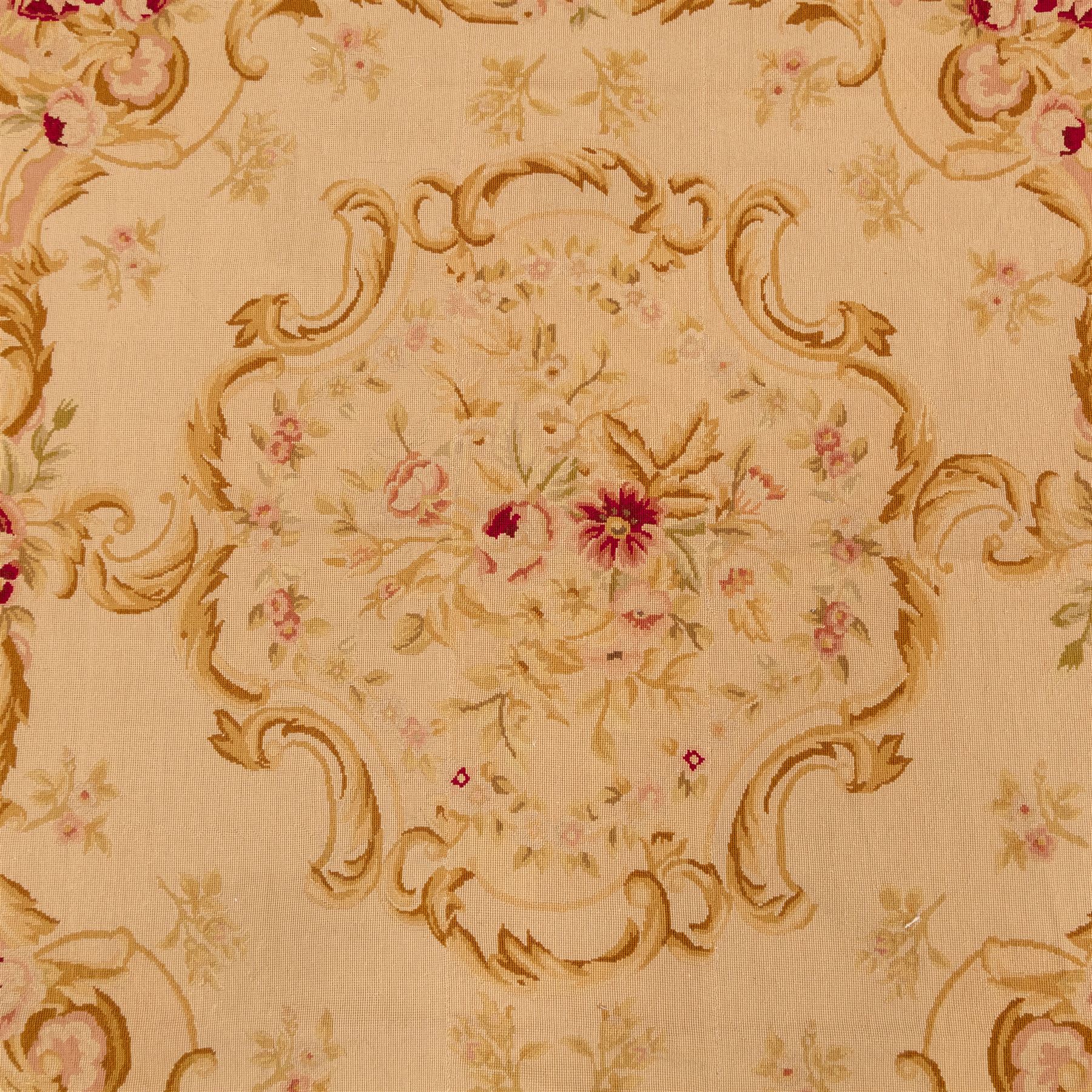 20th-century Aubusson-style tapestry wall hanging of square form, woven with a central floral medallion composed of delicate sprays in soft pinks, creams, and muted greens, framed by scrolling acanthus ornamentation and floral cartouches to each corner, all set within a pale ivory ground and enclosed by a terracotta toned border 