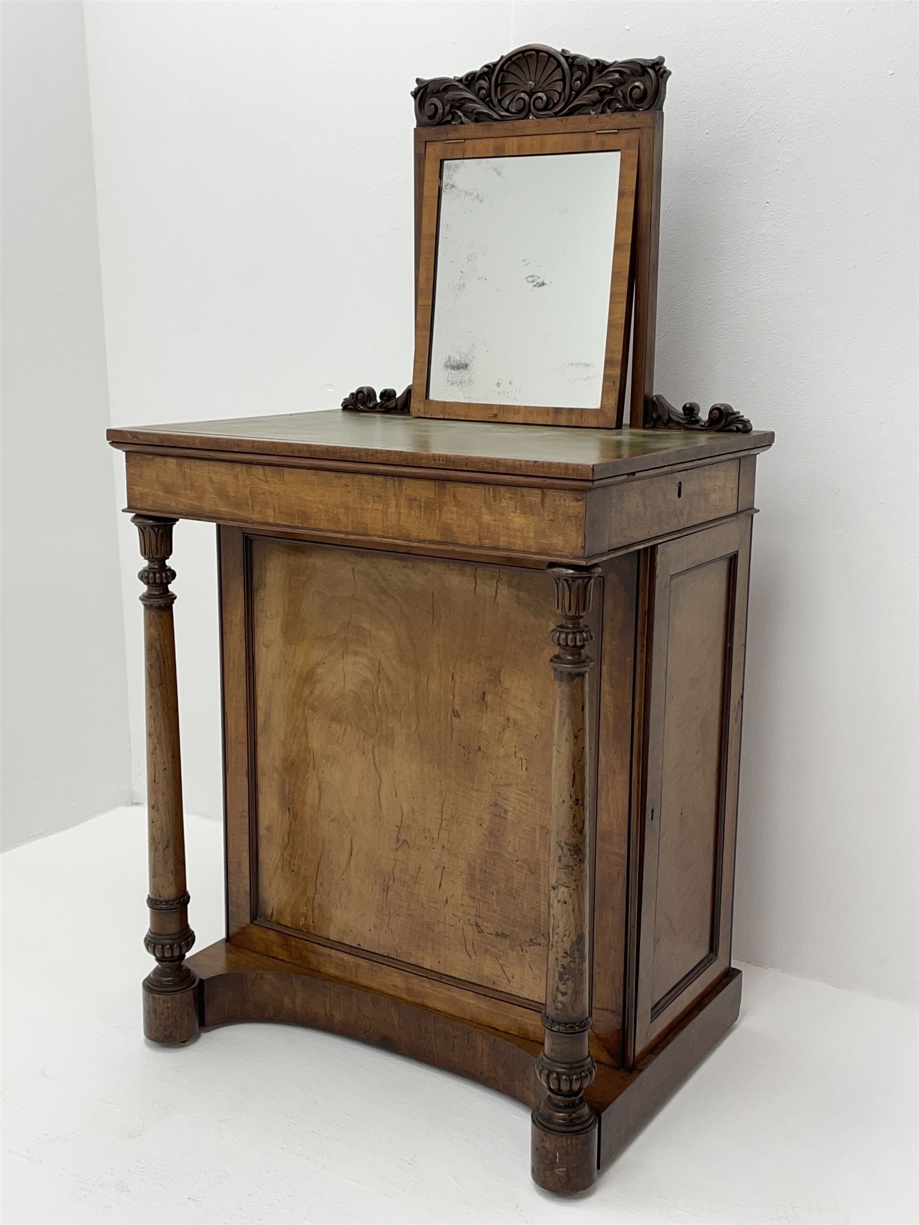 Early Victorian figured mahogany dressing cabinet, the raised shell and scroll carved back lifts to reveal rectangular easel mirror with mahogany band, flat rectangular top with tooled leather inset, slide at each side with matching leather inset, full width drawer above cupboard enclosing a series of five drawers, turned front supports, panelled front, sides and back