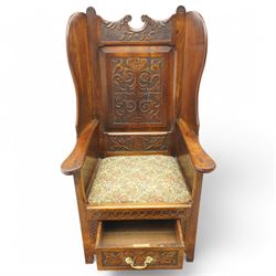 18th century design oak lambing chair, flower head and foliate carved cresting inscribed '1715' over panelled back carved with scrolling leafy branches, enclosed by shaped wingbacks over arms and panelled sides, the side panels carved with shells and scrolled leafage, upholstered seat over single drawer with matching carved decoration, on stile supports 