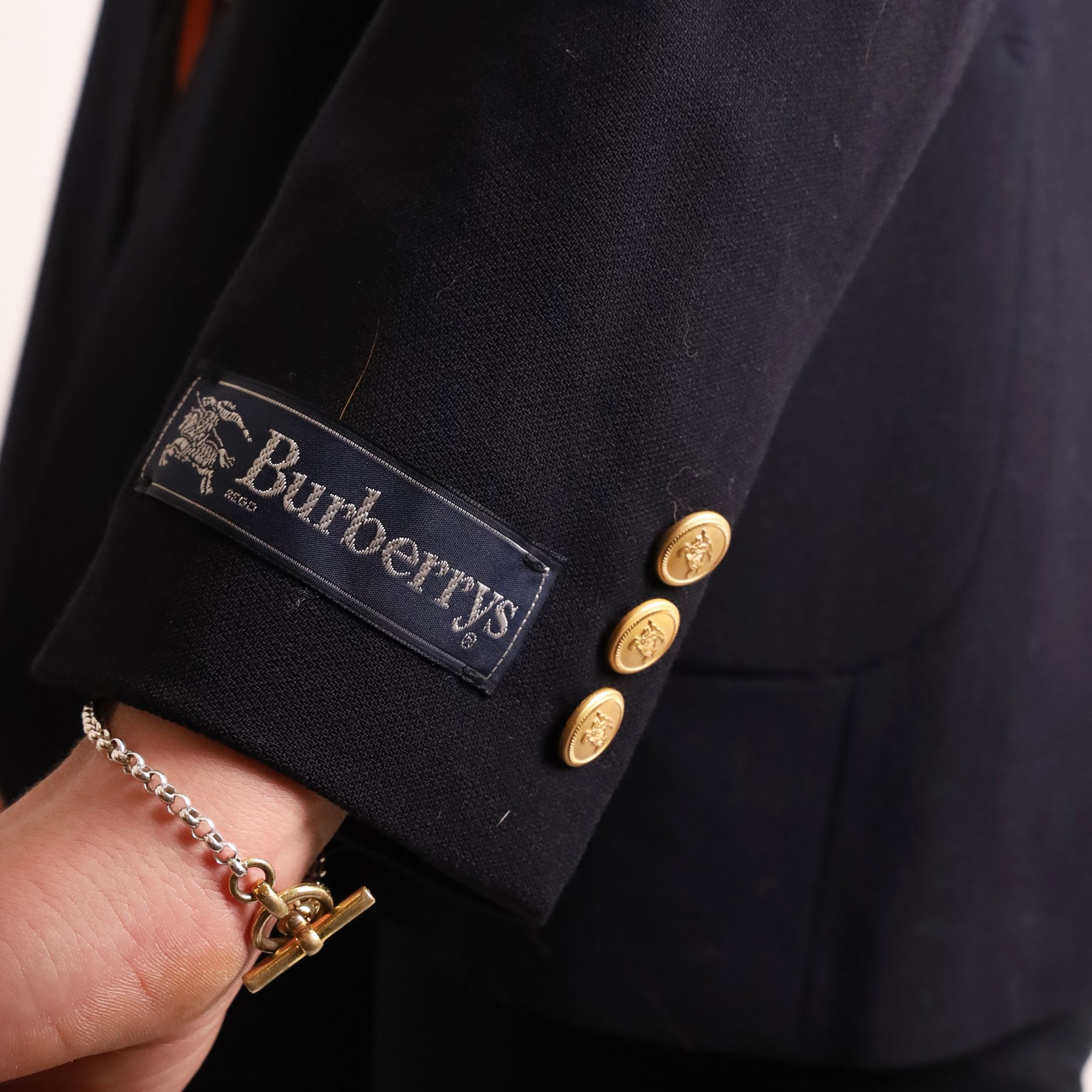 Burberrys – navy wool blazer and silk shirt, the blazer made in England, with gilt Burberry buttons, embroidered monogrammed breast pocket, black lining with Burberry motif and branded sleeve label, size S/M; the blouse in black 100% silk with all-over novelty print of keys, padlocks, coins and Burberry check motifs in yellow, orange and red, size S, made in Italy (2)