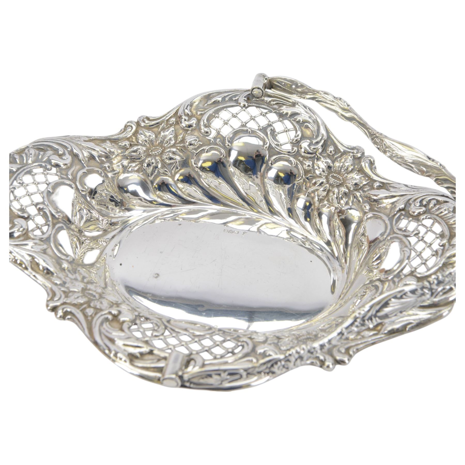 Edwardian silver swing handled basket, of oval form with shaped rim, embossed with floral decoration and with pierced latticework sides, upon four pad feet, hallmarked Chester 1905, maker's mark worn and indistinct