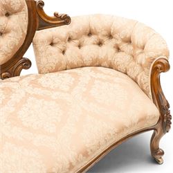 Victorian carved walnut framed double-ended settee with serpentine front, the central oval cameo back with flowerhead carved cresting rail, flanked by foliate C-scroll spandrels, the scroll carved arm terminals over floral carved cabriole supports with scroll feet and ceramic castors, the buttoned back and sprung seat upholstered in pale pink foliate patterned damask fabric