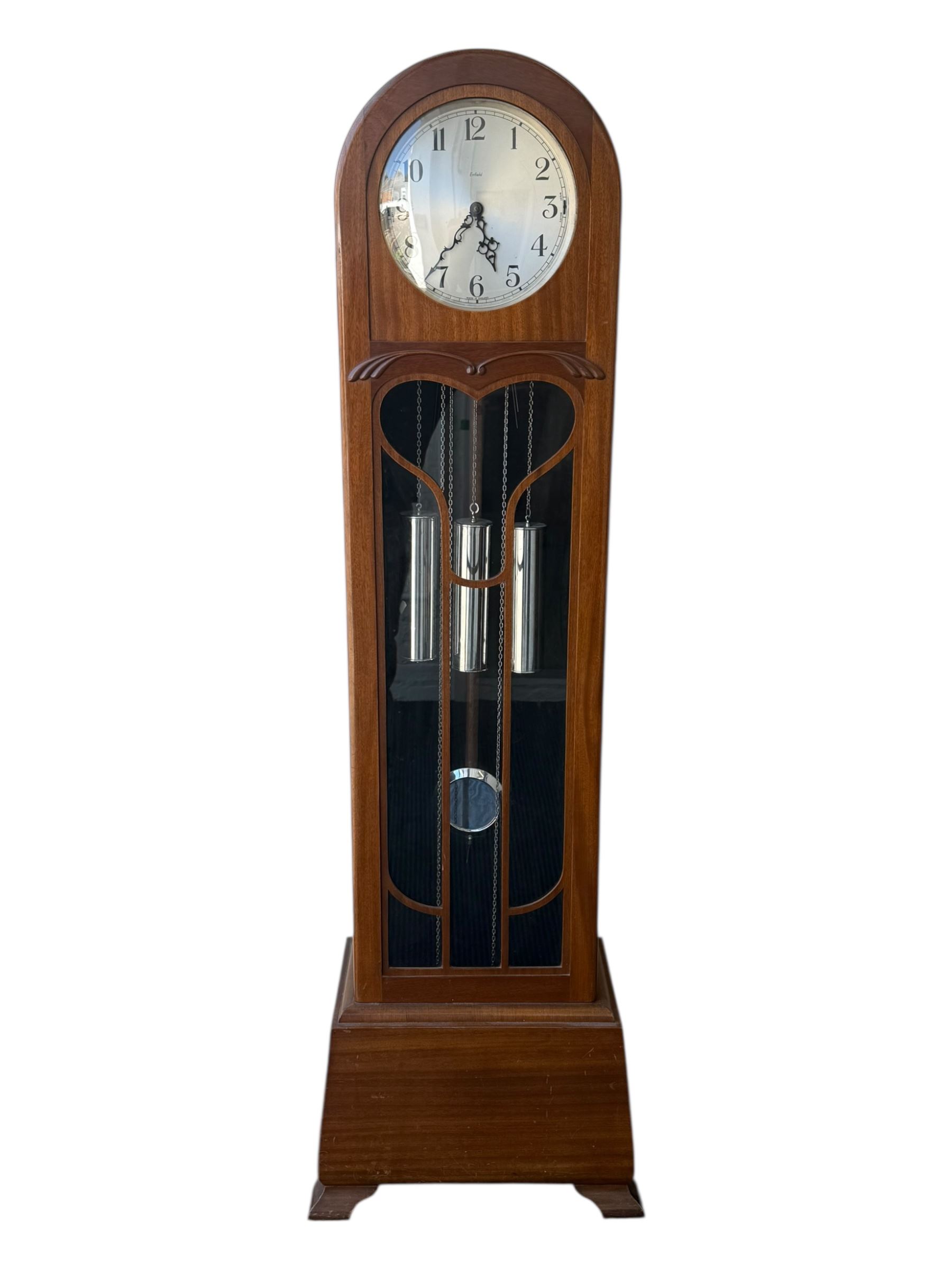 English- Art deco mahogany 8-day longcase clock, with an arched top and fill length fully glazed door beneath, on a short plinth with bracket feet, three train chain driven movement with visible stainless steel cased weights and pendulum, silvered dial with Arabic numerals, minute track and pierced steel hands, quarter chiming movement with  Westminster/ Whittington/ strike/silent selection.
