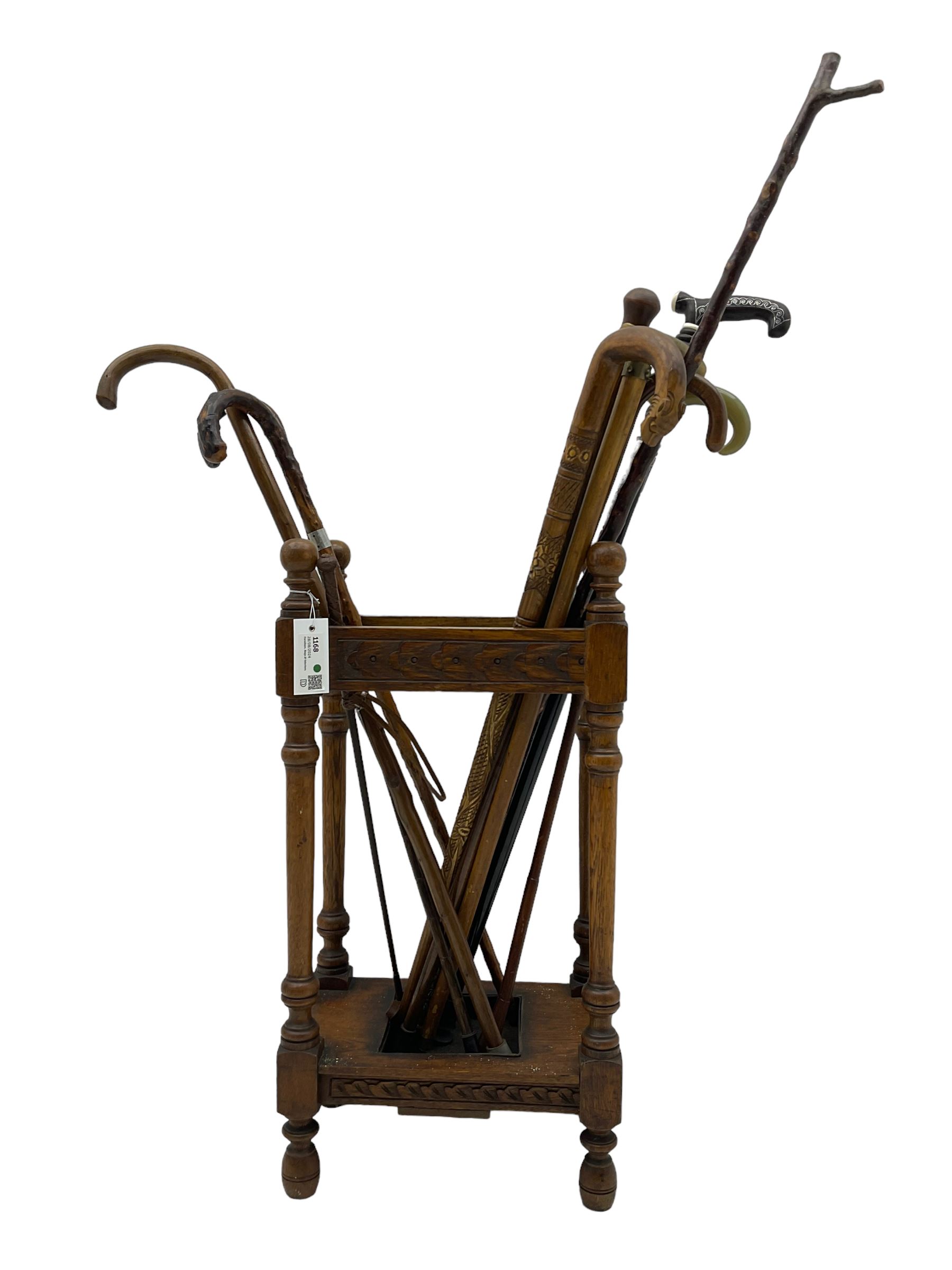 Early 20th century oak stick stand, rectangular structure with decorative carving, square base fitted with tray, on turned supports topped with finials; twelve assorted walking canes 