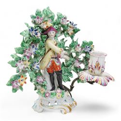 Pair of Bow porcelain 'New Dancers' candlesticks, standing before flowering bocages, and wearing brightly coloured flowered clothes, each supporting to left and right a tôle peinte branch terminating in a leaf moulded nozzle, on scrolling footed bases, red anchor and blue/red dagger marks beneath, H19cm x W18cm (2)