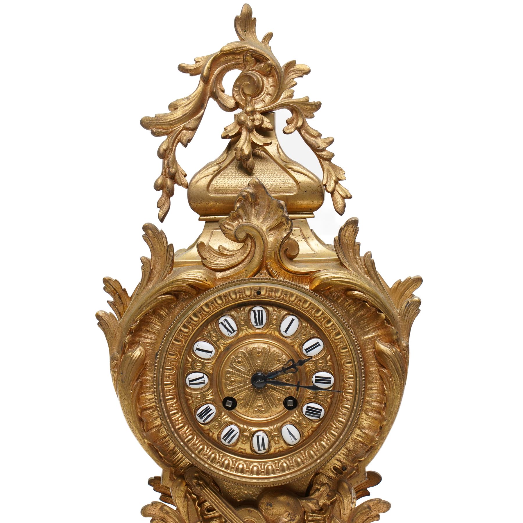 French-Late 19th century 8-day gilt brass rococo style mantel clock, c1890, waisted case  decorated with scroll work, leaves and musical instruments, resting on an attached plinth with splayed feet, dial within a glazed brass bezel with a gilt repoussé centre, porcelain cartouche Roman numerals and steel fleur-di-Lis hands, with a twin train movement, recoil anchor escapement and countwheel strike, sounding the hours and half-hours on a bell. With a matching pair of five-light candelabra. No Pendulum or Key.