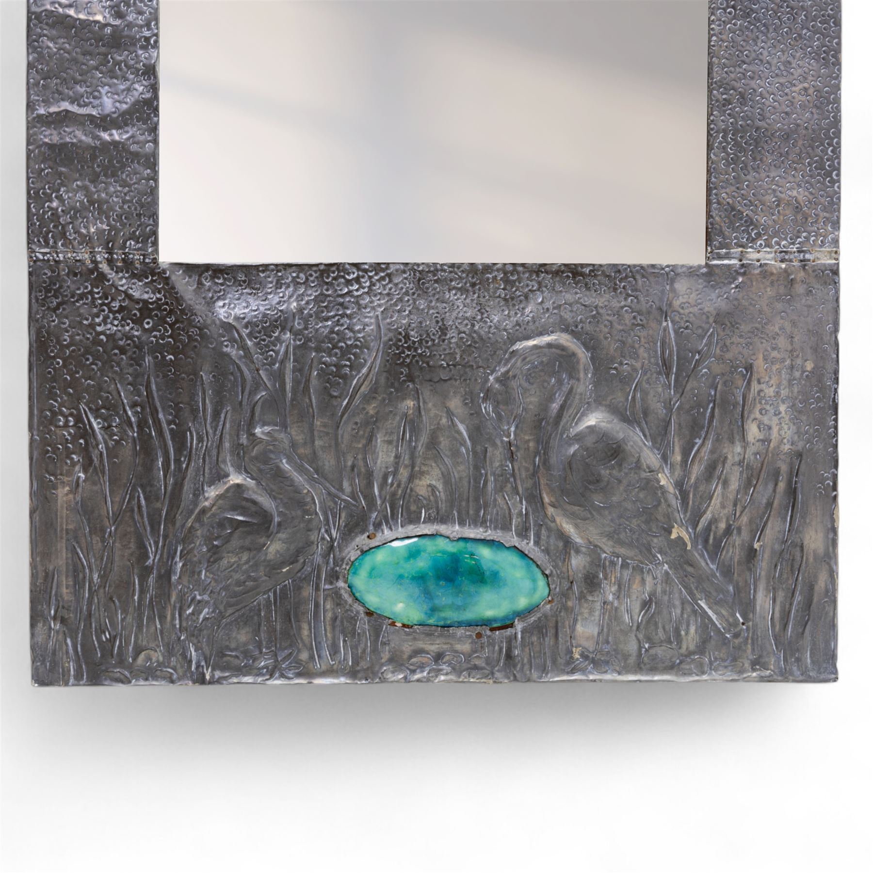 Early 20th-century Arts and Crafts pewter wall mirror, rectangular bevelled mirror plate within a punched pewter frame repoussé decorated with herons among reeds, with a central inset green enamel cabochon panel
