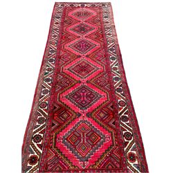 Persian Hamadan red ground rug, decorated with six stepped lozenge medallions, the guarded border with repeating stylised flower head decoration, with inscription to corner
