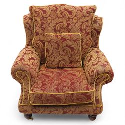 Duresta – pair of armchairs, upholstered in red and gold damask fabric with piped edges, scroll arms and loose feather-filled cushions, raised on turned wooden feet with brass castors