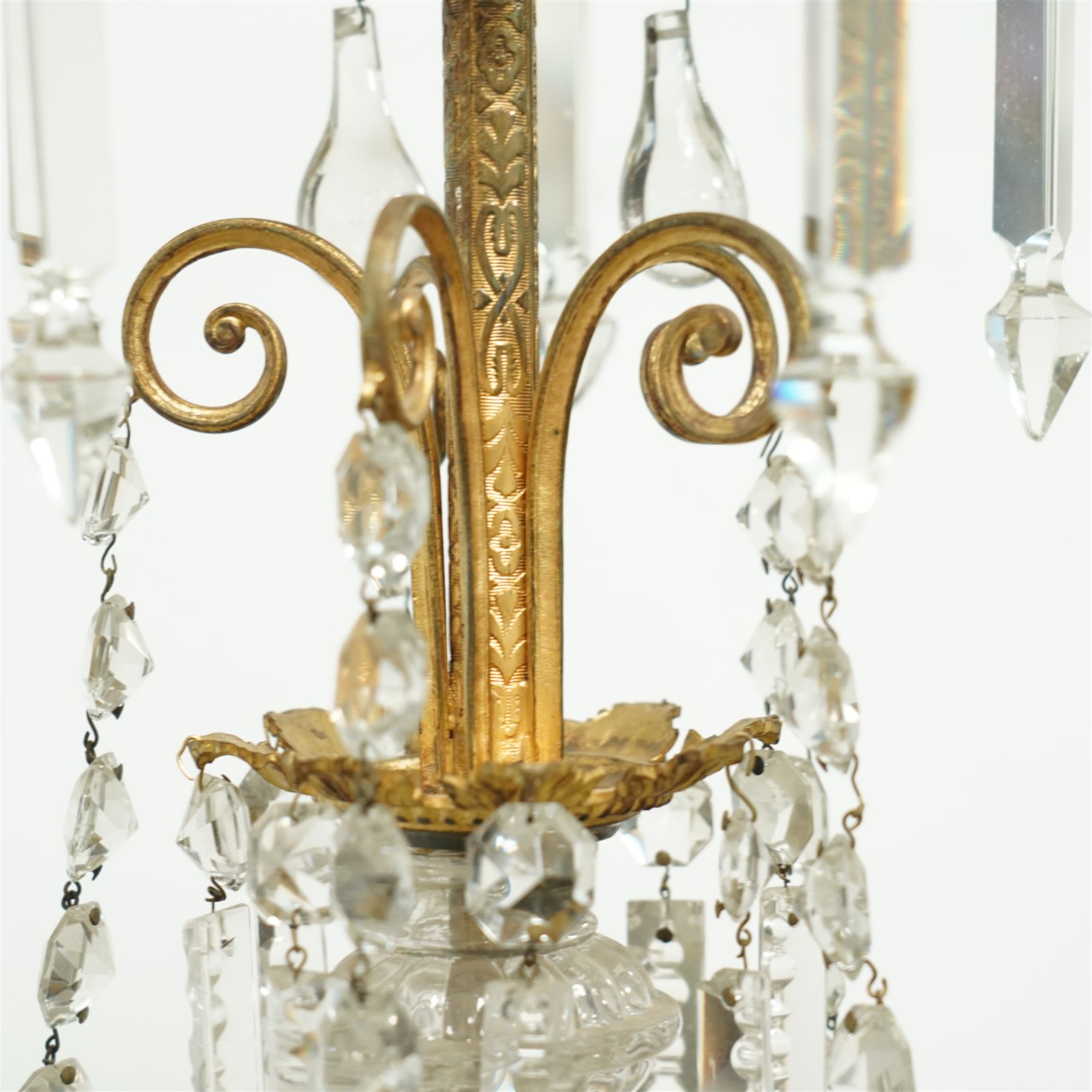 Late Victorian gilt bronze mounted crystal chandelier, ceiling rose above shaped top of trailing swags, glass crystal droplets, beneath rising curled branches and glass beads tapering down to five candle sconces, inside circular bezel fitted with drops and glass twist fluted stem, supported with an internal metal shaft above a rococo style stem holding double branches, and similar styled branches, with twelve branches fitted with candle holders and drip trays with crystal drops and cut crystal spears, the underside festooned with crystal glass swags and a bulbous fluted glass terminal and shaped finial with crystal glass swags attached to the branches, the base with pear shaped droplet graduating to the centre, wired for electricity 
