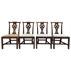 Set four late Georgian mahogany dining chairs, shaped cresting rail with carved ears over Chippendale style splat, pierced and carved with scrolls and interlocking lozenge, upholstered drop in seats, on square supports joined by plain stretchers