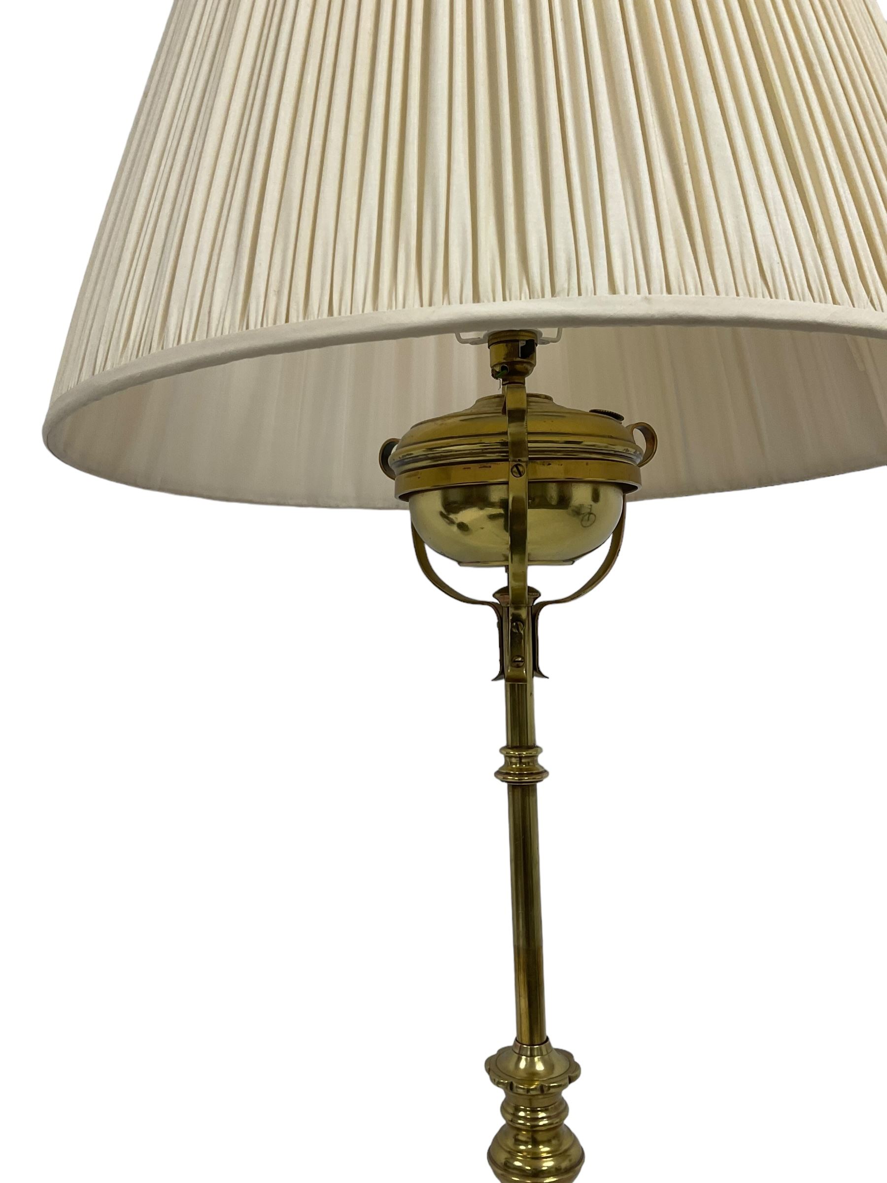 Edwardian brass plated copper standard lamp, telescopic stem on lobe moulded circular base with three projecting paw feet, with cream shade
