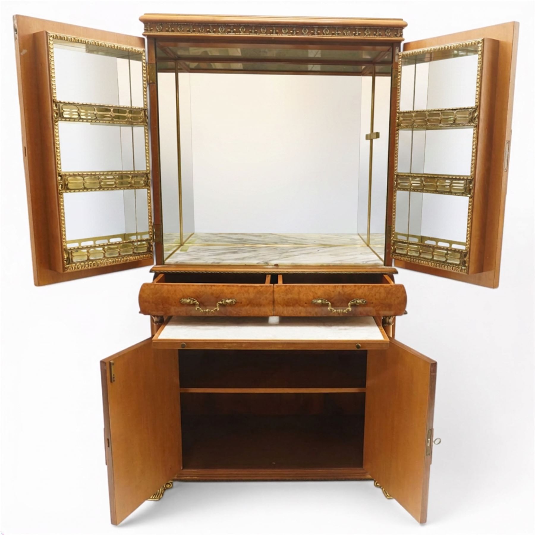 Early 20th century Art Deco burr maple mirrored drinks cabinet, rectangular top with gilted cornice, twin cabinet doors with gilt escutcheons, enclosing a mirrored interior with shelves behind the doors, marble base to the top section above two short drawers over a marble inset slide, the lower cabinet with cabinet doors flanked by pilasters, raised on gilted bracket feet 