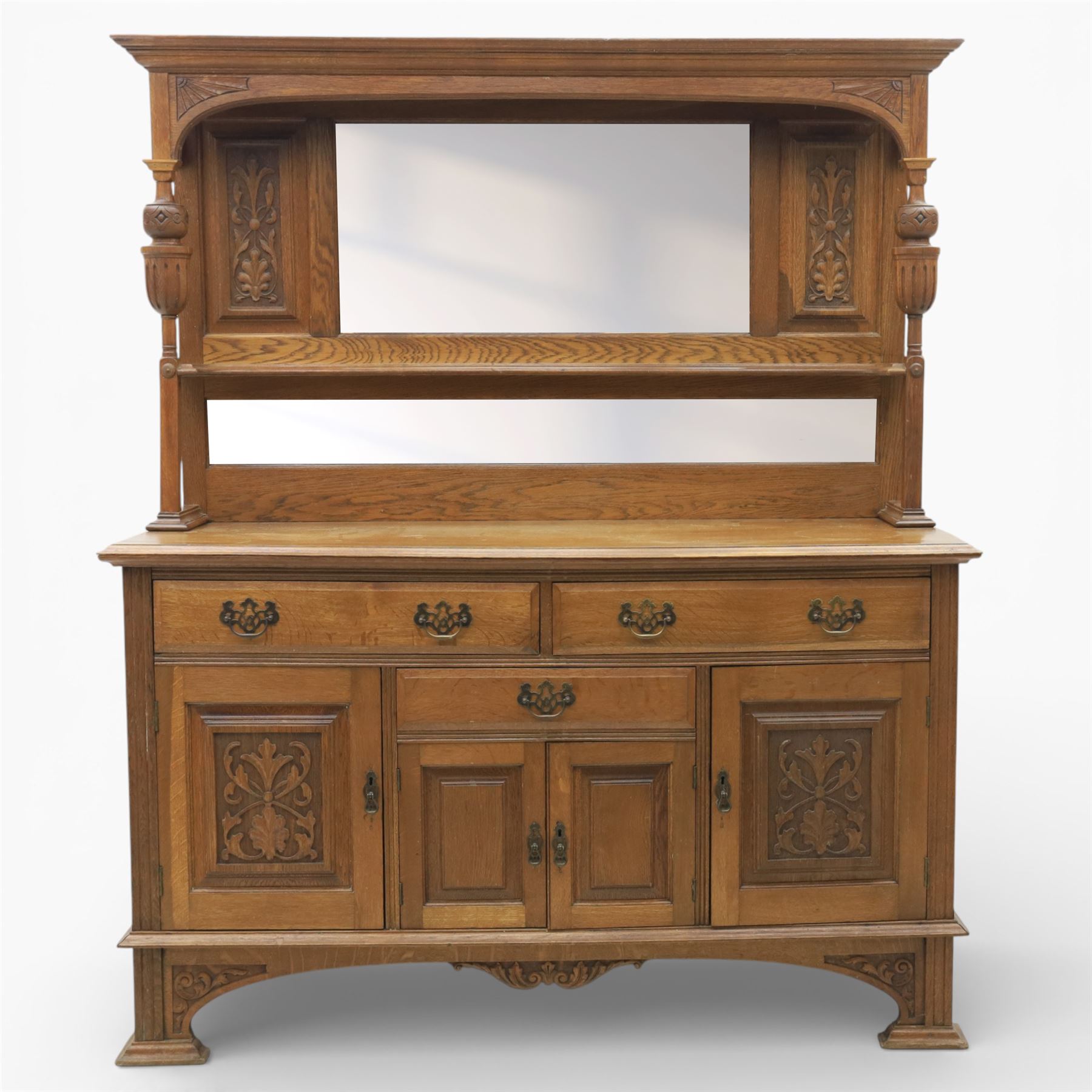 Arts and Crafts oak mirror back sideboard, the bevelled rectangular mirror set within a back with foliate carved panels, with turned baluster and knopped supports, upon a base with moulded top above three drawers  and three cupboard doors, two with carved foliate detail, upon four shaped bracket feet