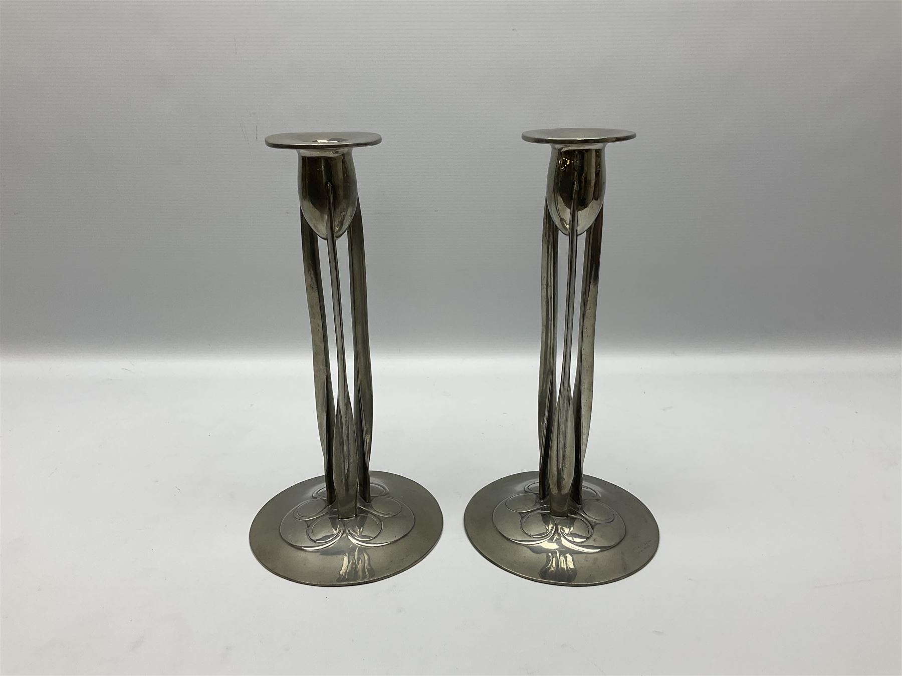 Archibald Knox (1864-1933) for Liberty & Co, pair of Tudric pewter candlesticks, the bud shaped sockets raised upon three angular fin supports and a slightly domed circular base with cast stylised foliate decoration, each stamped beneath Tudric 0223, H30cm