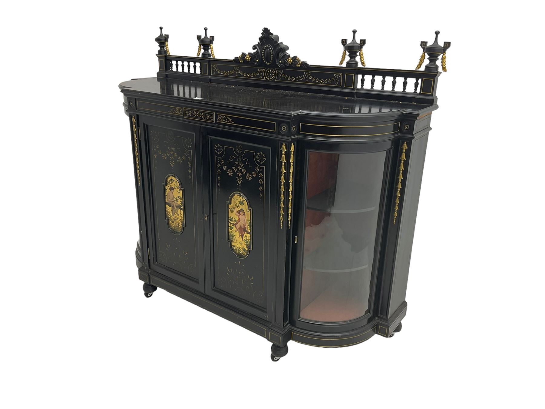 Victorian ebonised credenza side cabinet, raised balustrade back with urn finials and a central carved cartouche, carved and gilded with floral garland decoration, central doors with gilt panels painted with figures sitting over a lake enclosing two shelves, flanked by applied bellflower detail and glazed bow-front side doors, raised on ring turned feet with castors