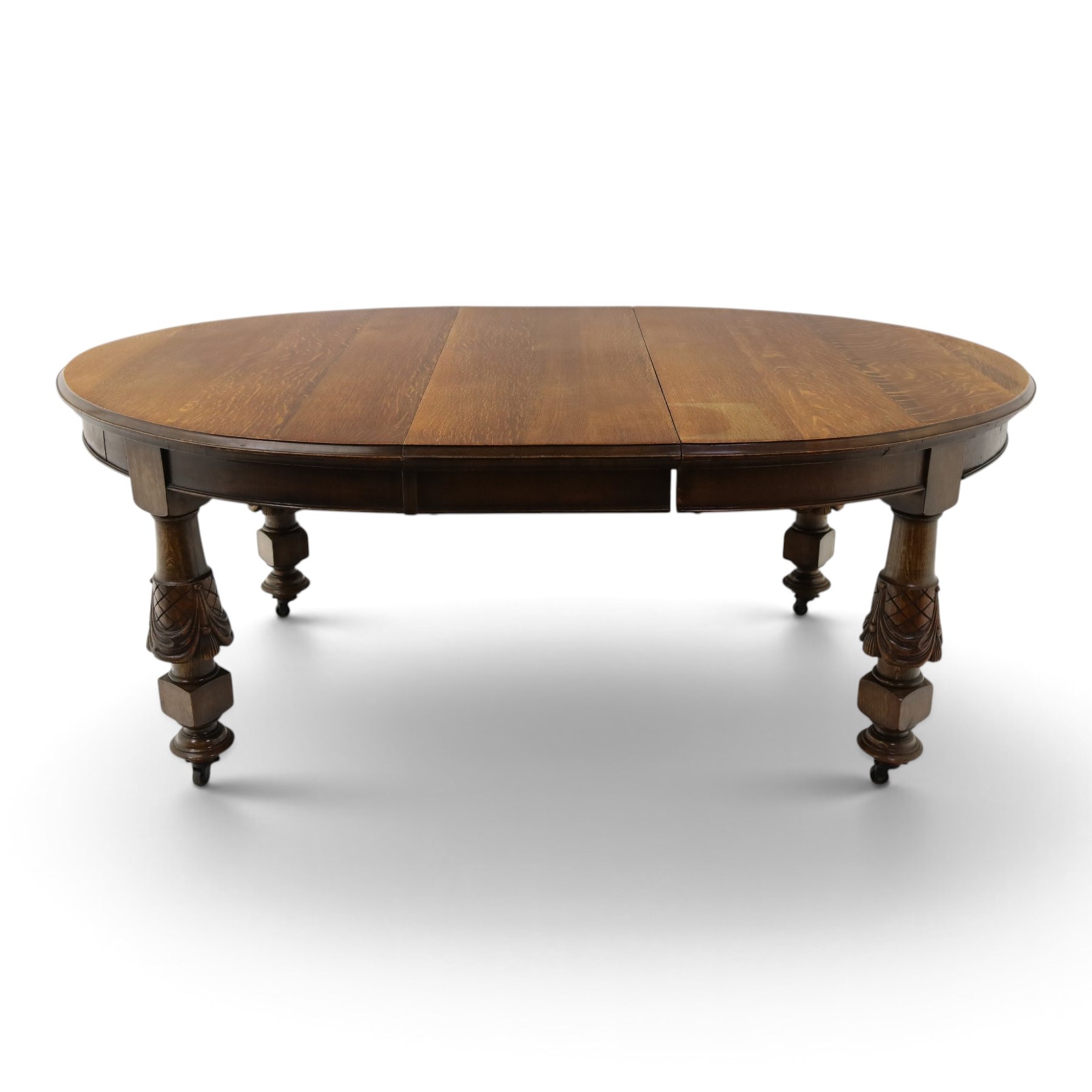 Late 19th century French oak extending dining table, oval top with moulded edge and plain frieze, raised on four ornate carved supports decorate with carved latticework and large festoons with tassels, on turned feet, with two additional leaves