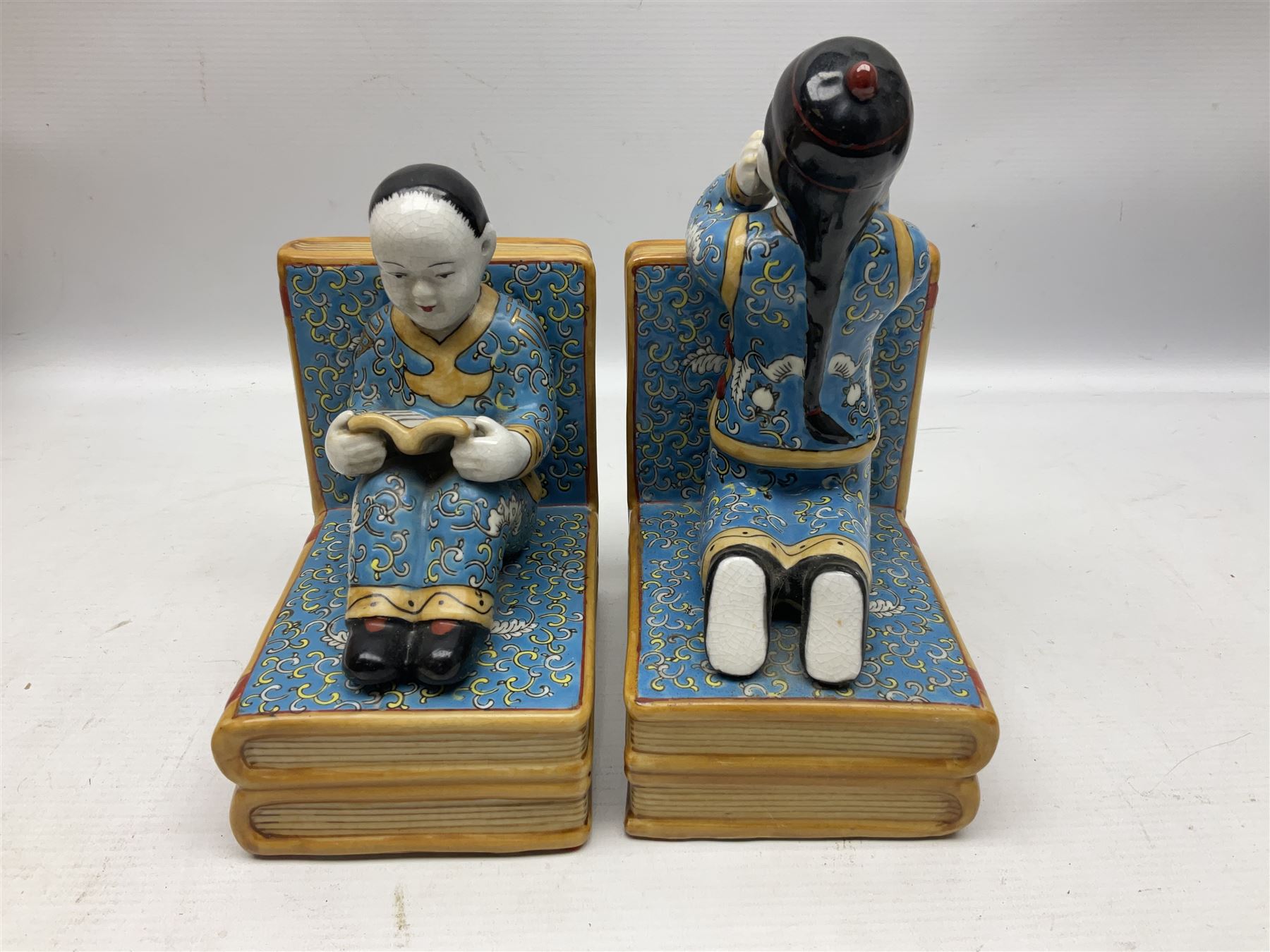 Pair of 20th century Chinese figural bookends, modelled as children in traditional blue dress sat reading and kneeling upon stacks of books, H22cm