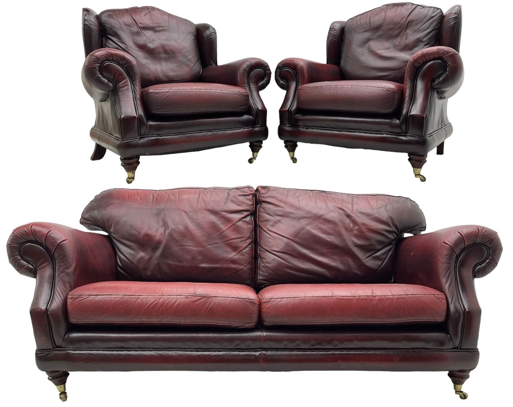 Thomas Lloyd - three-piece lounge suite, comprising of traditional shape two seat sofa (W190cm H80cm) and a pair of wingback armchairs (W100cm H91cm), each with rolled arms over turned supports with brass castors, upholstered in oxblood red leather