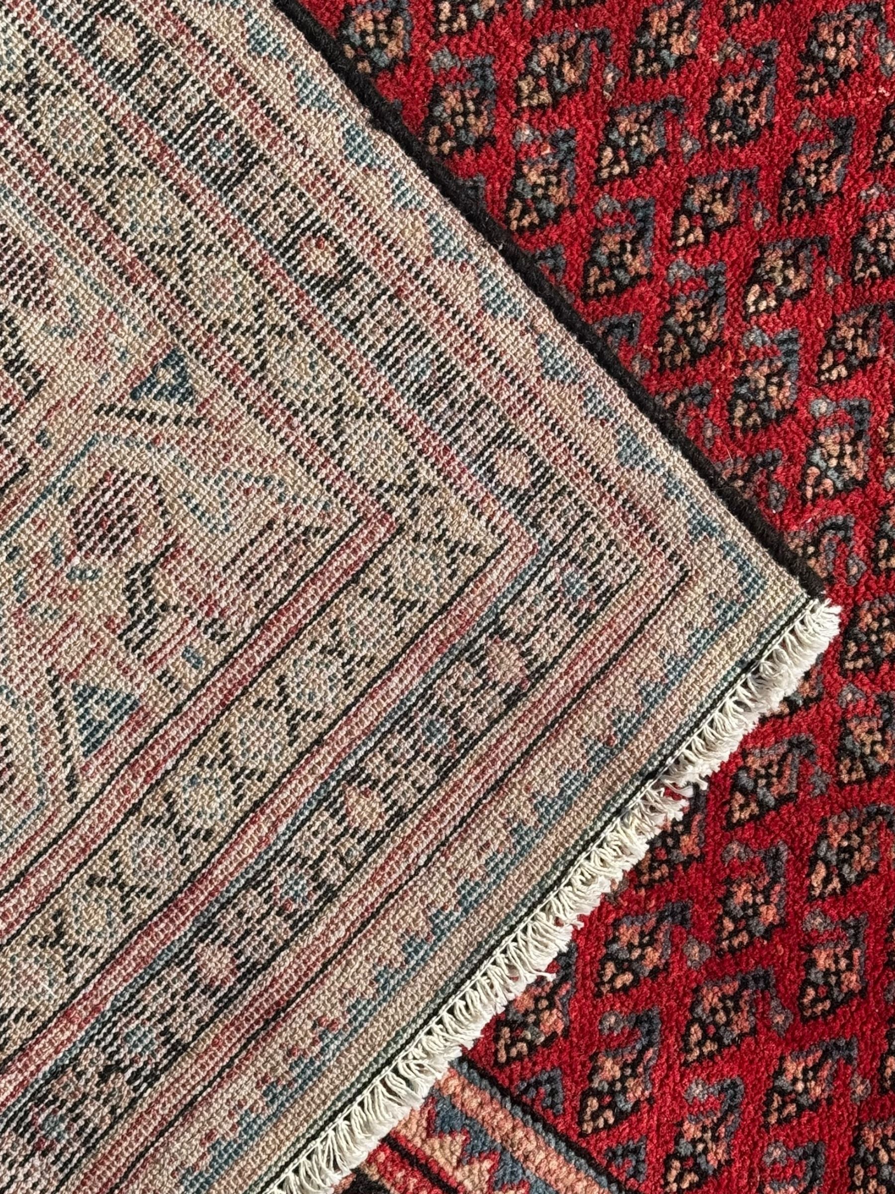 Persian Arak crimson ground rug, the field decorated with repeating Boteh motifs within geometric guard stripes