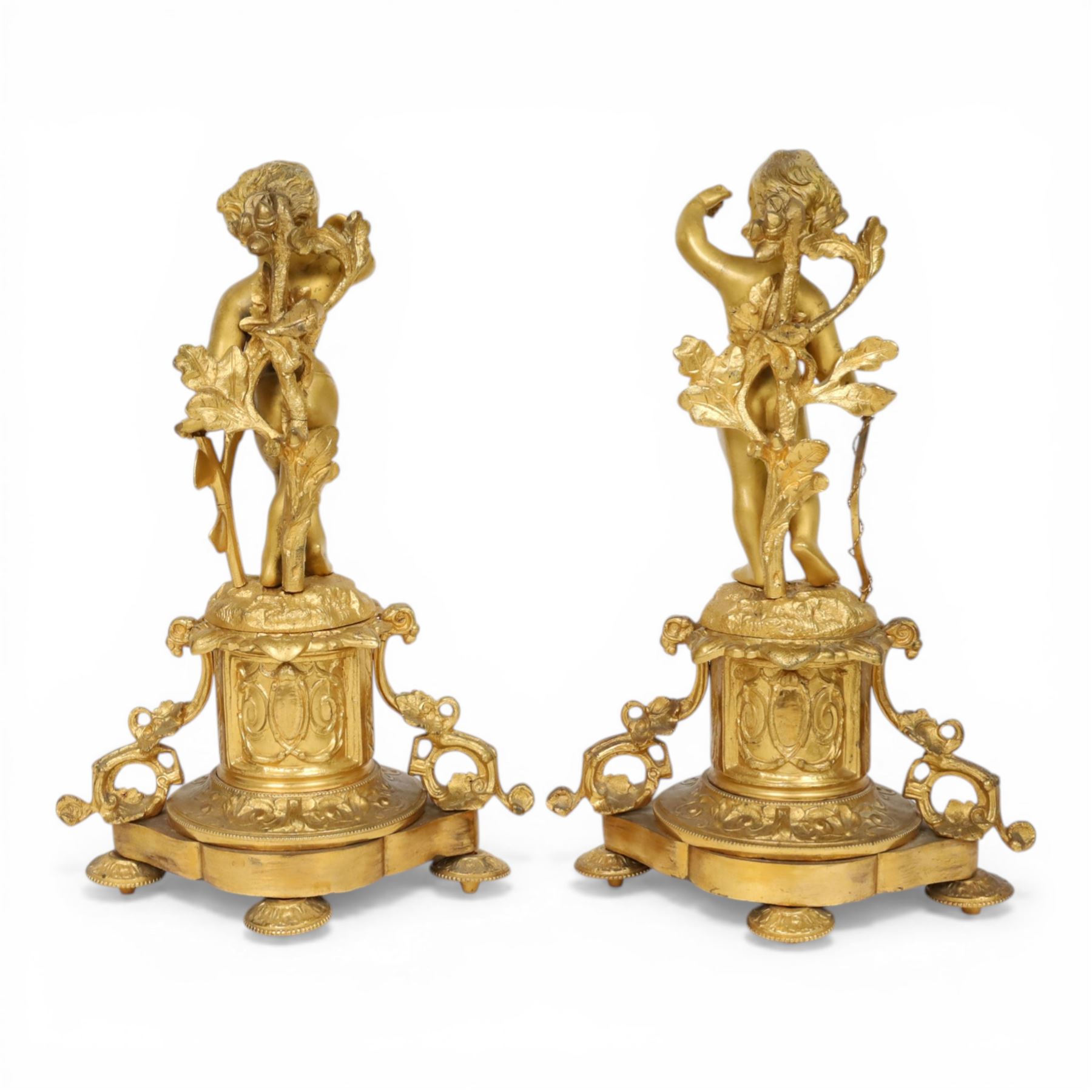 Pair of 19th century ormolu putto figures, each modelled stood with foliate support to backs, upon a naturalistic base upon cylindrical plinth each with twin leafy tendril supports, each plinth with inset Sevres type painted panel of a cherub, upon a shaped base with four compressed disk feet, the front facing with leaf mount, H29cm