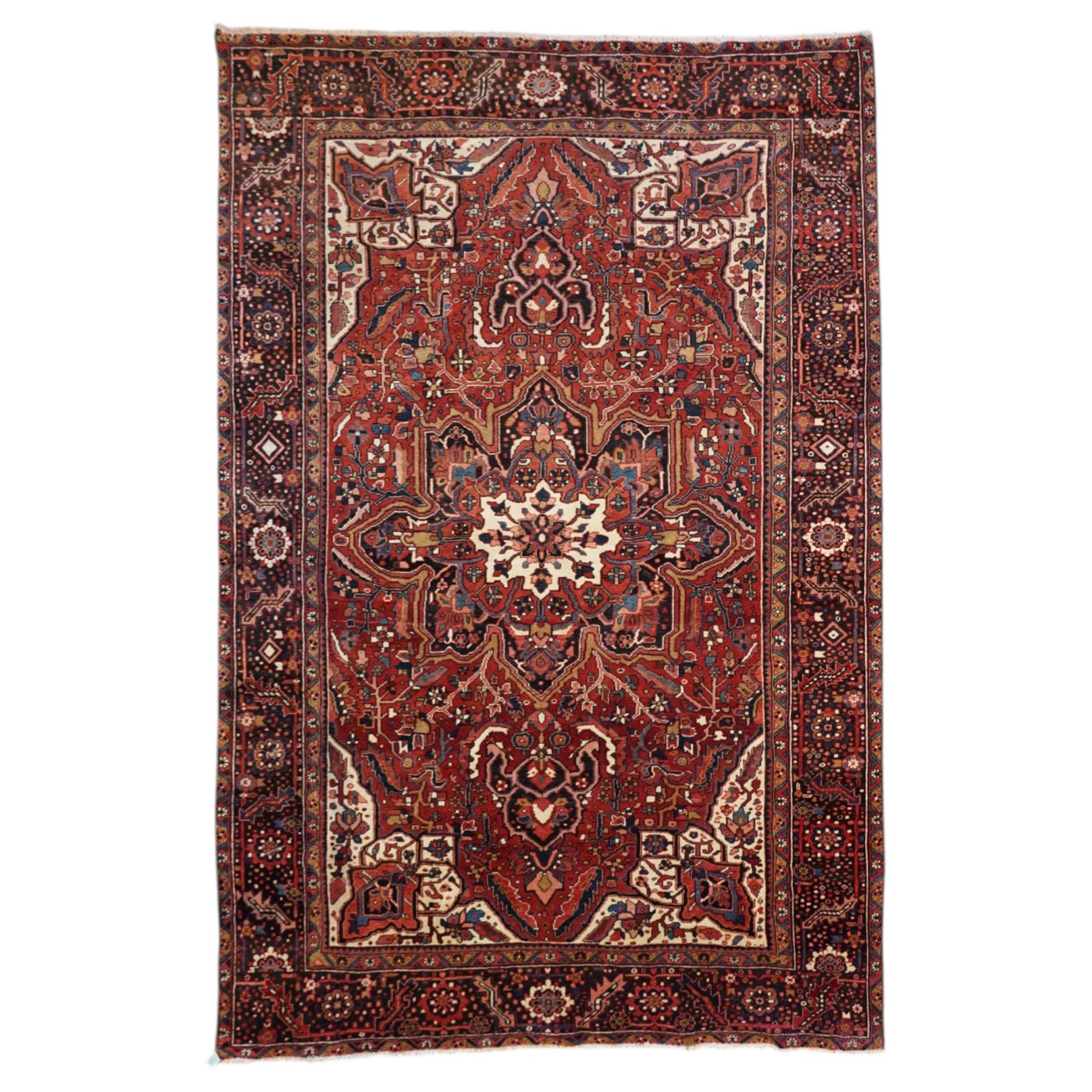 North West Persian Heriz/Ahar hand-knotted carpet, brick red field with a central bold stepped star medallion with pendants, surrounded by angular floral and geometric motifs, ivory spandrels, enclosed by a dark indigo border of stylized rosettes and vine motifs with multiple guard stripes, cotton fringe ends 