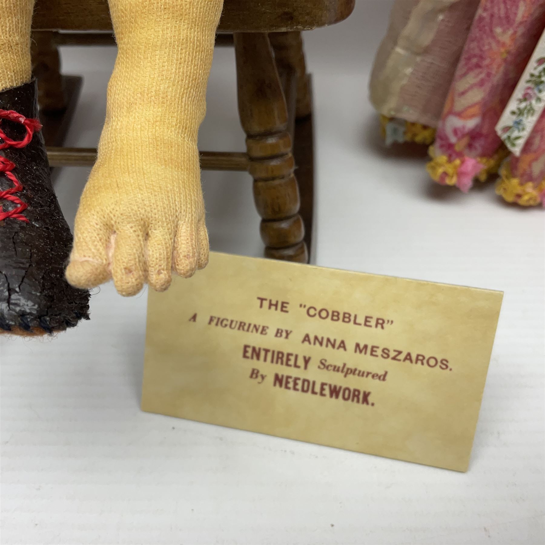 Anna Meszaros Hungary - three hand made needlework figurines - 'The Cobbler' as a child seated in a wooden rocking chair working on a removed boot H28cm; young girl in a long floral dress standing playing a harp H35cm; and young girl wearing a blue tabard standing playing a lute (3) Auctioneer's Note: Anna Meszaros came to England from her native Hungary in 1959 to marry an English businessman she met while demonstrating her art at the 1958 Brussels Exhibition. Shortly before she left for England she was awarded the title of Folk Artist Master by the Hungarian Government. Anna was a gifted painter of mainly portraits and sculptress before starting to make her figurines which are completely hand made and unique, each with a character and expression of its own. The hands, feet and face are sculptured by layering the material and pulling the features into place with needle and thread. She died in Hull in 1998.  