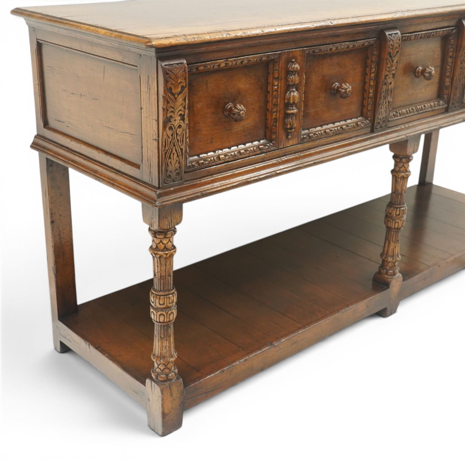 Titchmarsh & Goodwin - Tudor oak dresser base, three drawers flanked by foliate carving and carved wooden knobs, on turned and carved supports, united by a full length undertier