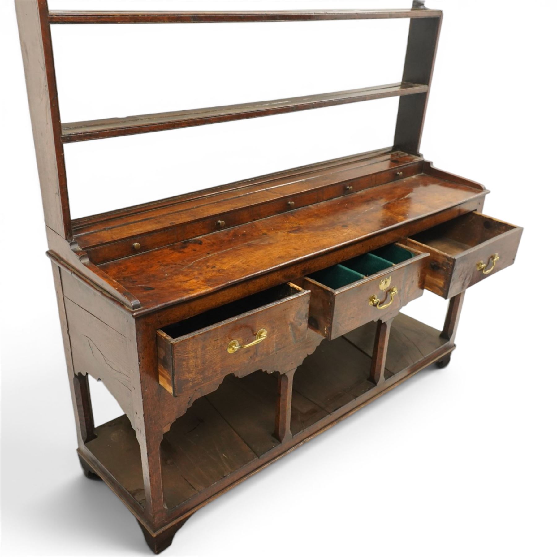 18th century Georgian oak dresser base with plate rack, the three-tier plate rack with shaped frieze, the base with rectangular top with raised back fitted with five spice drawers, over three drawers with brass swan neck handles, raised on six square chamfered supports united by undertier 