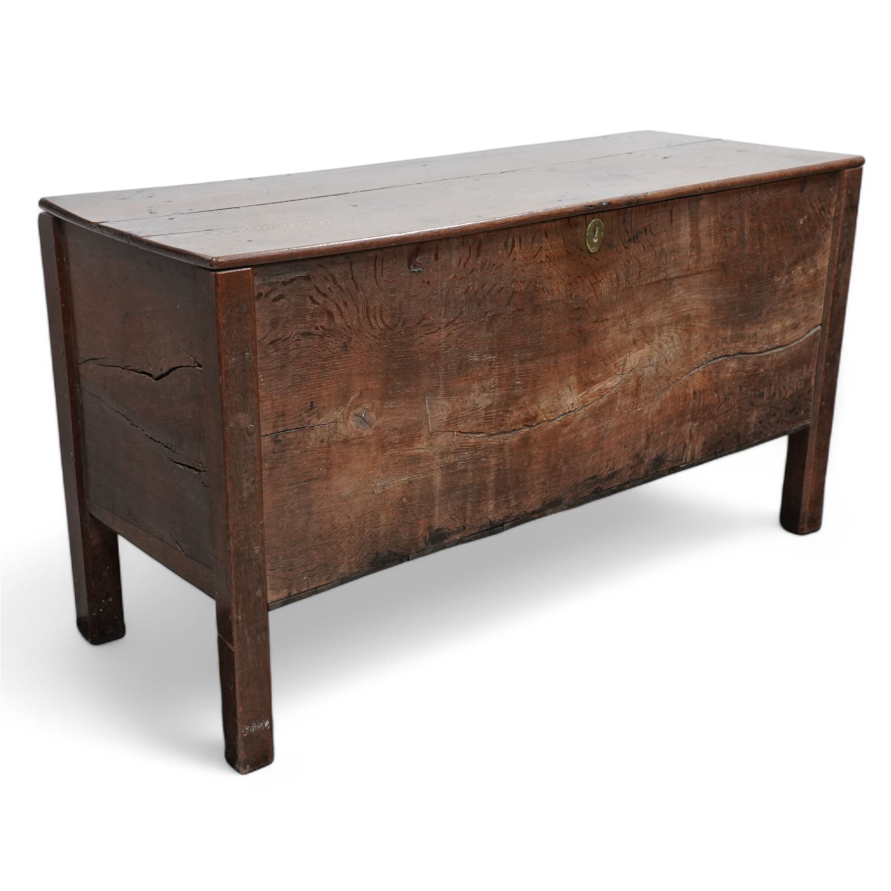 Large late 17th Century oak coffer, the hinged lid with twin rear strap hinges above a plain front with inset brass escutcheon, raised on square supports with pegged joinery and displaying pronounced grain figuring to the single front board