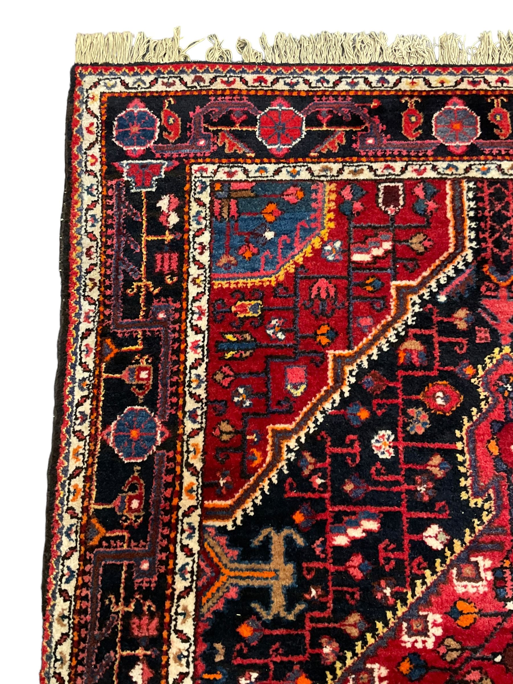 Persian Hamadan red and indigo ground rug, central lozenge medallion with extending poles, the field decorated with interlaced branches and flowerheads, guarded border with stylised floral motifs