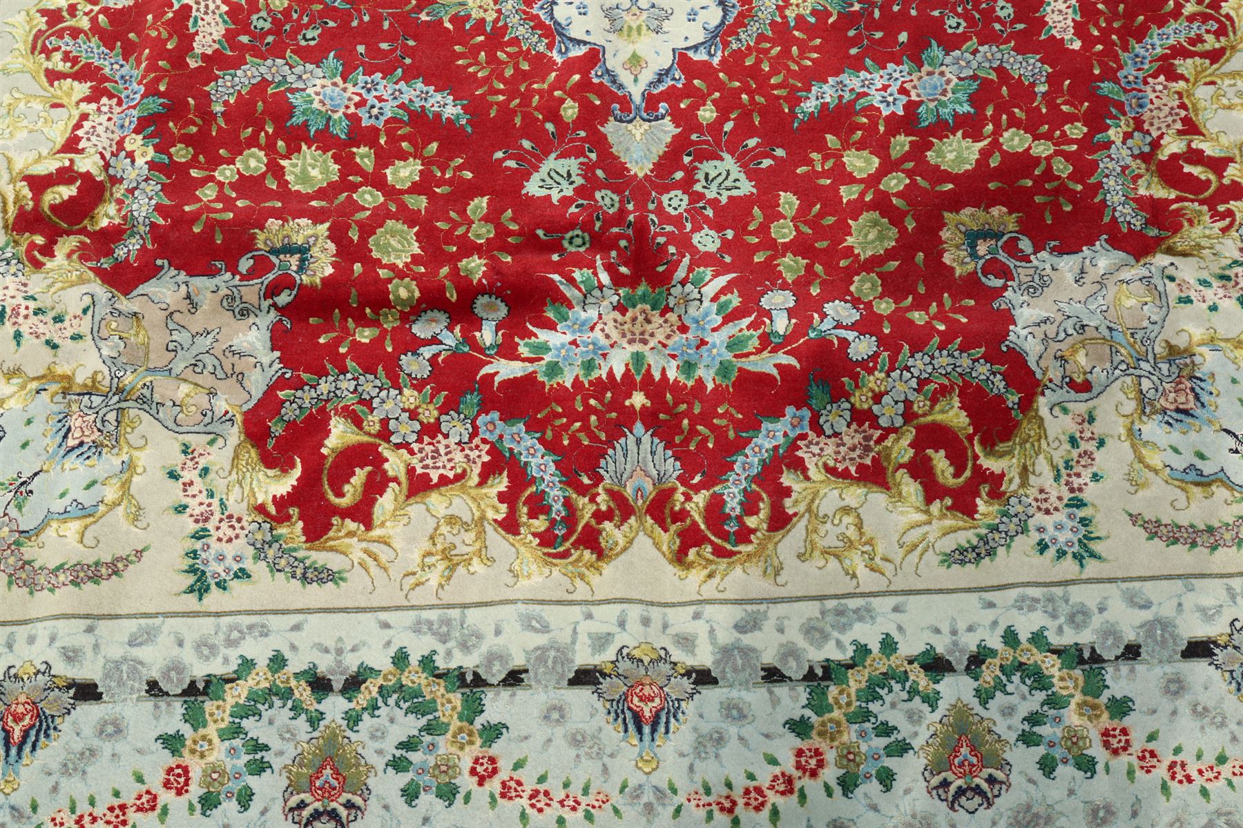 Persian silk inlaid crimson ground Kashan rug, the central shaped field with a floral pole medallion surrounded by trailing floral motifs and festoons of flowerheads, the wide cyan guard line with repeating palmettes and scrolling floral vines
