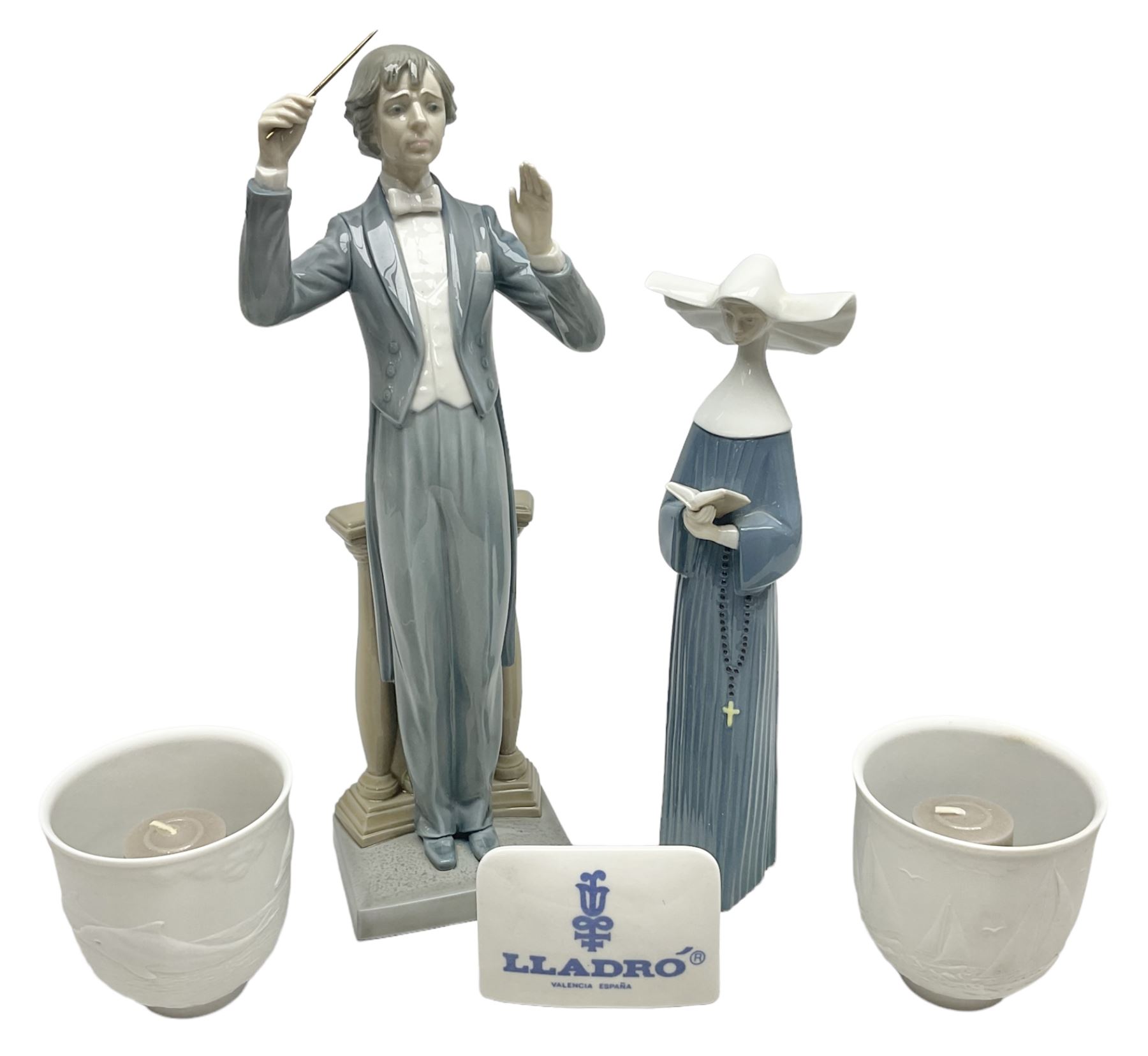 Two Lladro figures, comprising Conductor no 5196 and Prayerful Moment no 5500 together with a Lladro plaque and two Lladro candle holders, Dolphins at Play no 17666 and Sailing the Seas no 17665, all with original boxes, largest example H33cm 