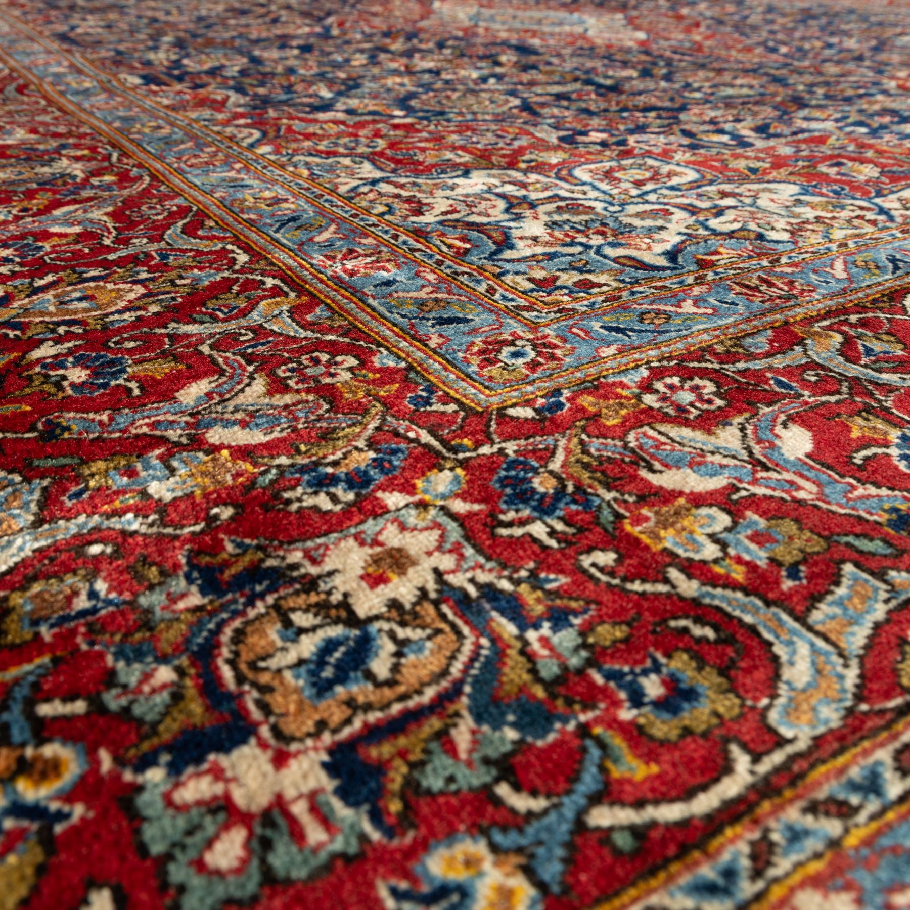 Persian Kashan carpet, navy field with central red diamond medallion enclosing floral rosette, framed by dense scrolling foliage and palmettes, triple borders in red, blue and ivory, originating from central Iran