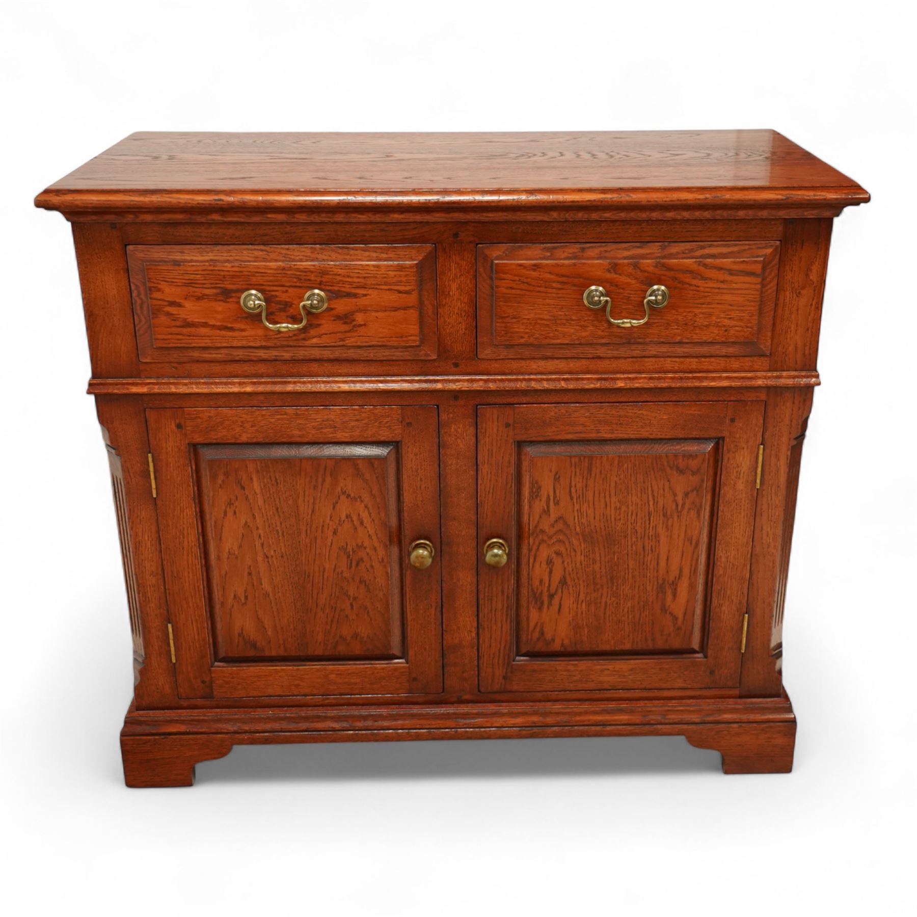 20th century country oak side cabinet, rectangular top over two short drawers and twin panelled cupboard doors, flanked by reeded uprights, on plinth base