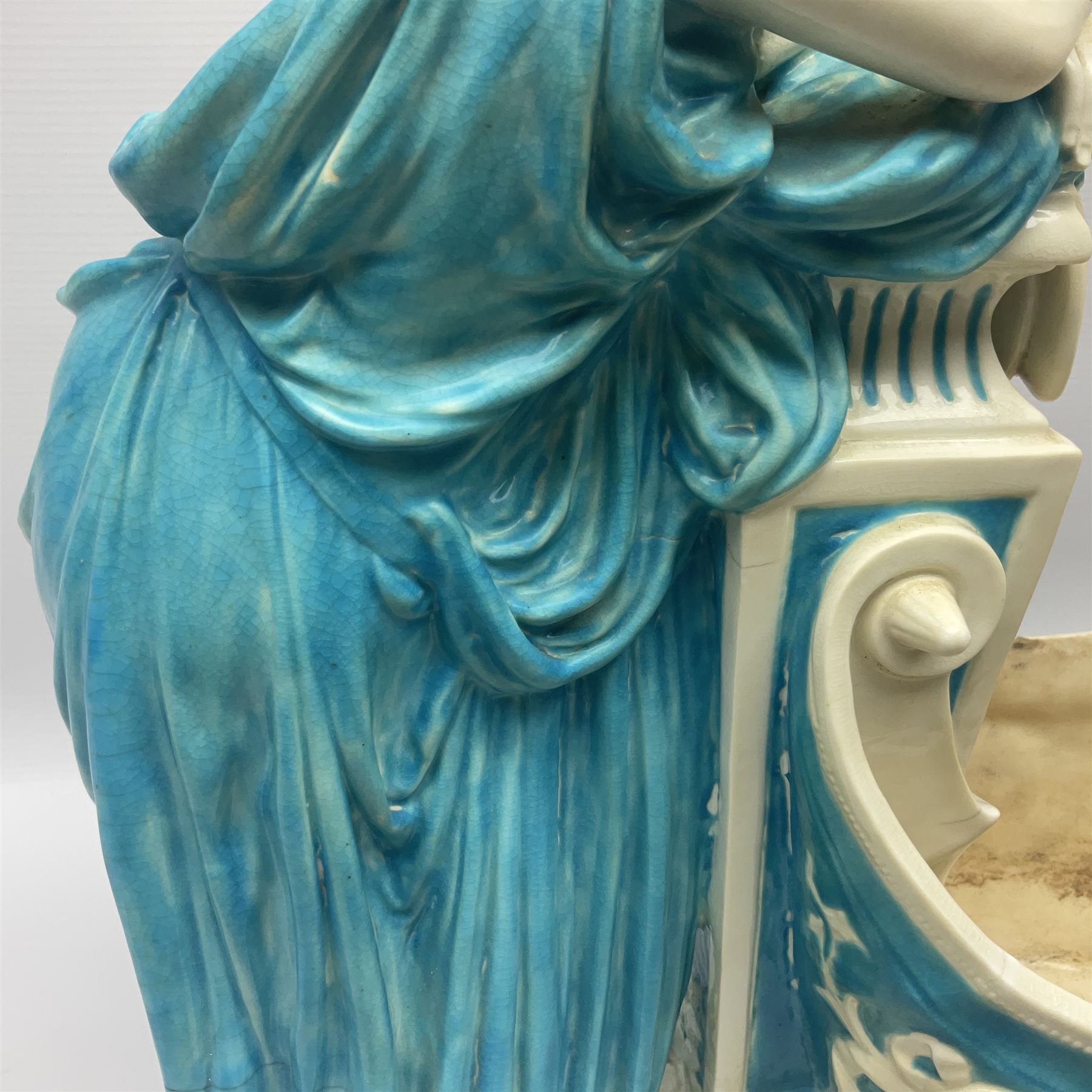 Rare 19th century Minton turquoise glaze majolica 'The Reader' flower holder, after Albert Carrier-Belleuse, modeled as a maiden in classical drapery reading whilst leaning against the pillar back of the helmet shaped cistern detailed with a caryatid and floral swags, the whole upon an oval plinth with Greek key border, with impressed marks beneath, H44cm