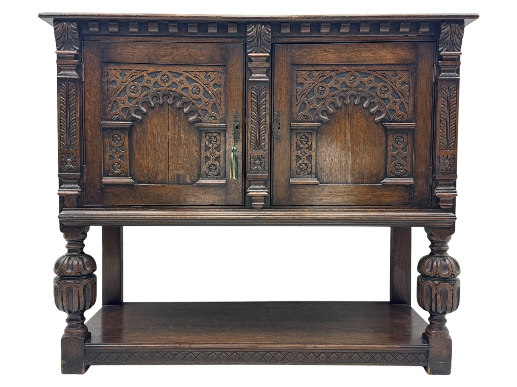 Jacobean design carved oak two door cupboard, the frieze and twin cupboard doors carved with arcaded panels and stylised foliage, raised on baluster supports united by an undertier