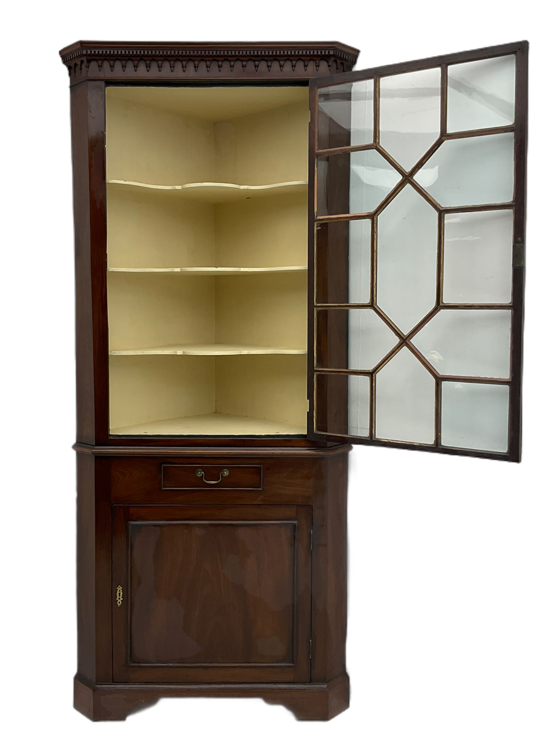 George III mahogany floor standing corner display cabinet, dentil cornice, upper astragal glazed door above small drawer and lower cupboard, on bracket feet, in two sections
