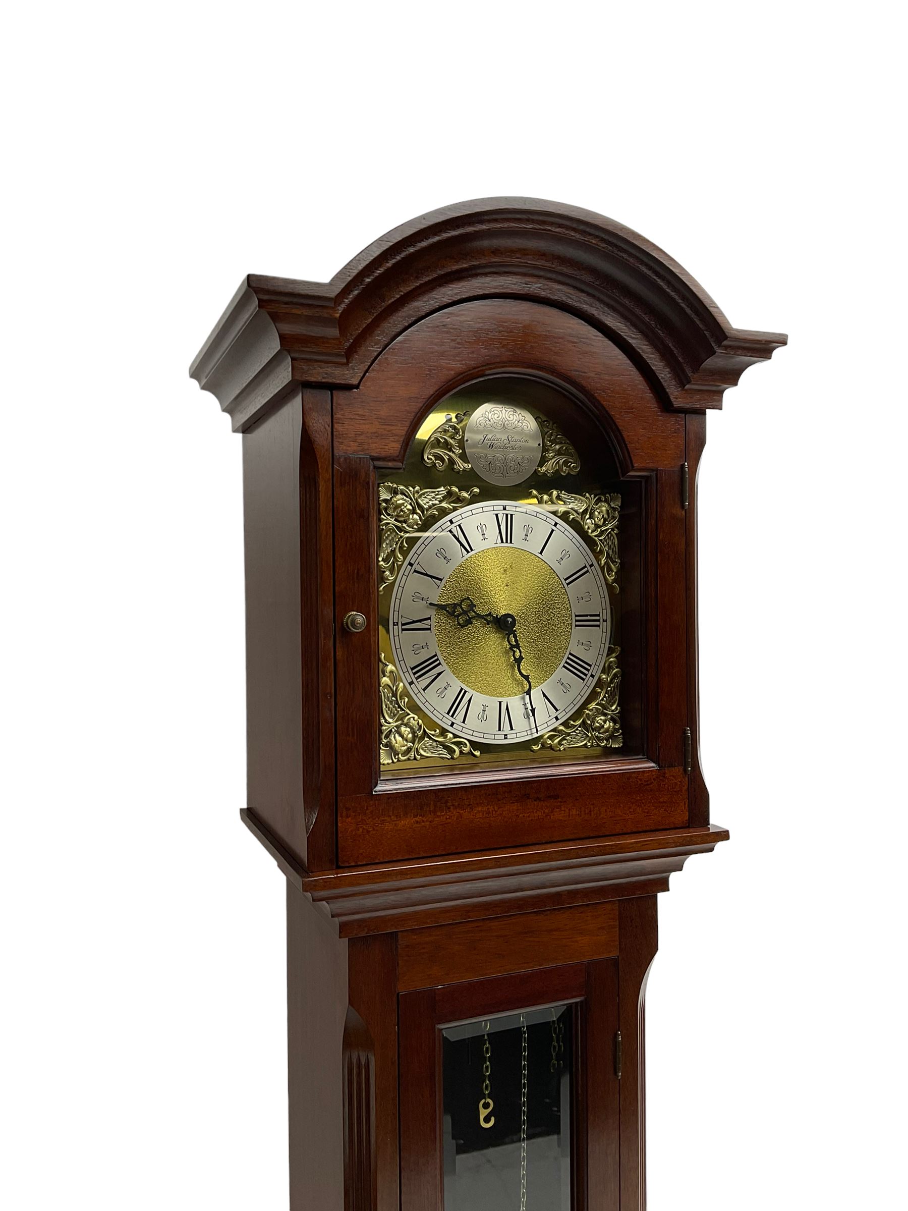 Mahogany cased Grandmother clock c 1980 made and retailed by Julian Stanton, Winchester, with a break arch pediment and corresponding brass dial, full length glazed door displaying three brass cased weights and pendulum, raised on a square plinth with a recessed panel and skirting, German Kieninger three train chain driven movement striking the hours and quarters on 12 gong rods. With weights and pendulum.  