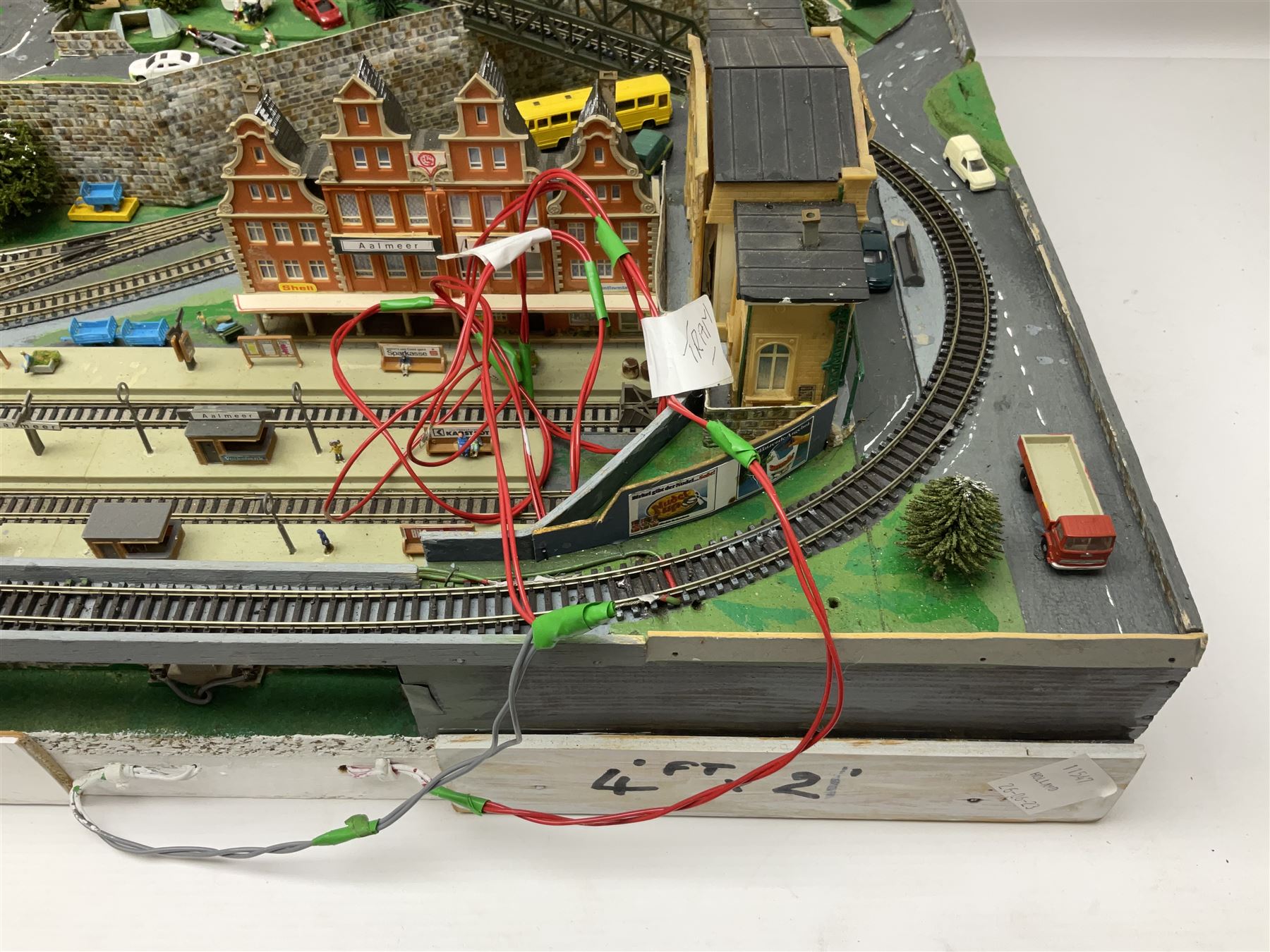 Table top 'N' gauge continental scenic layout as a split level town with various loops of track, station with numerous platforms, engine shed, assorted buildings, roads with motor vehicles and figures, tunnels, trees, river with bridge, tram depot etc 122 x 52cm